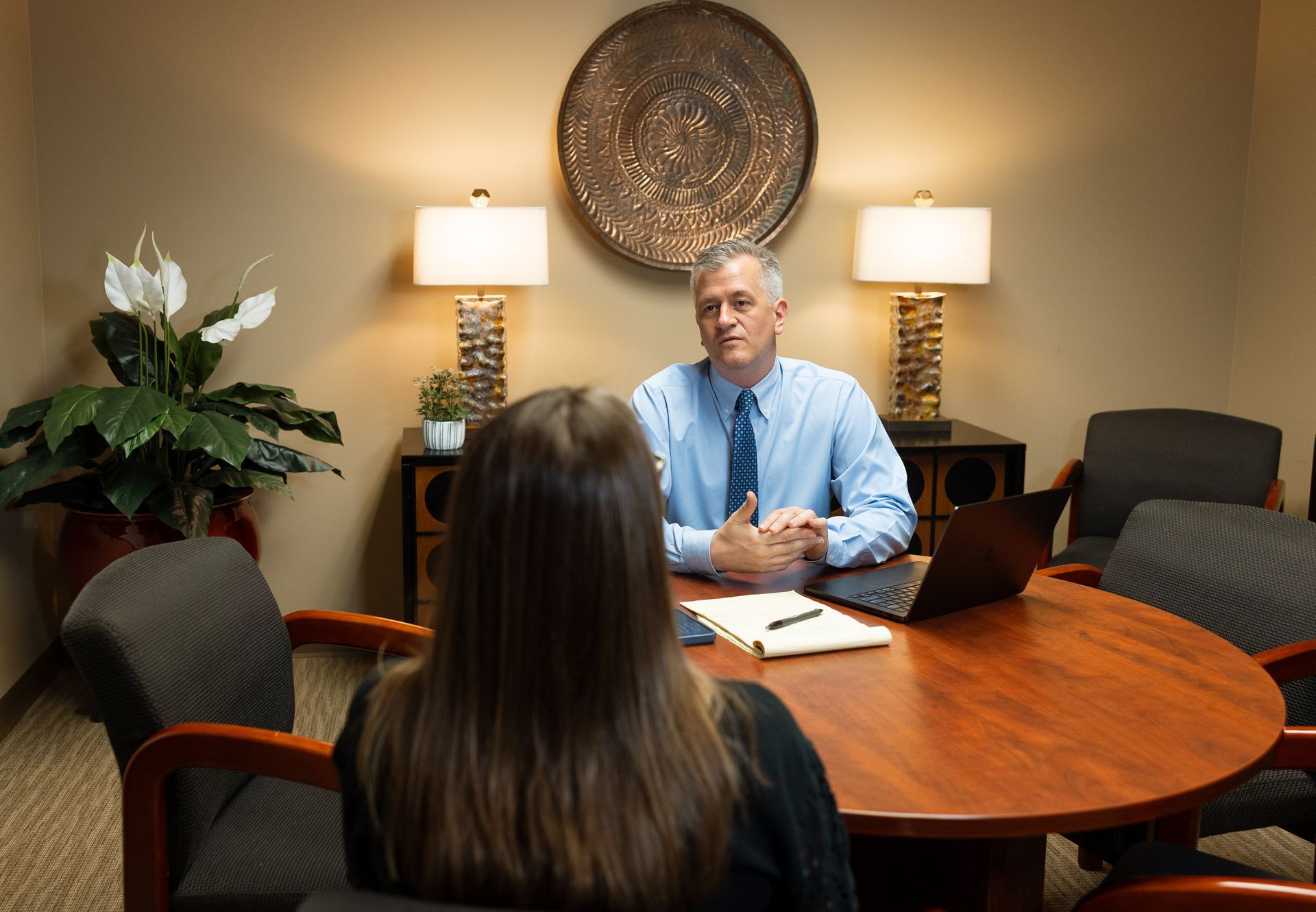 Two people in a conference room having a meeting around a wooden table with laptops and papers.