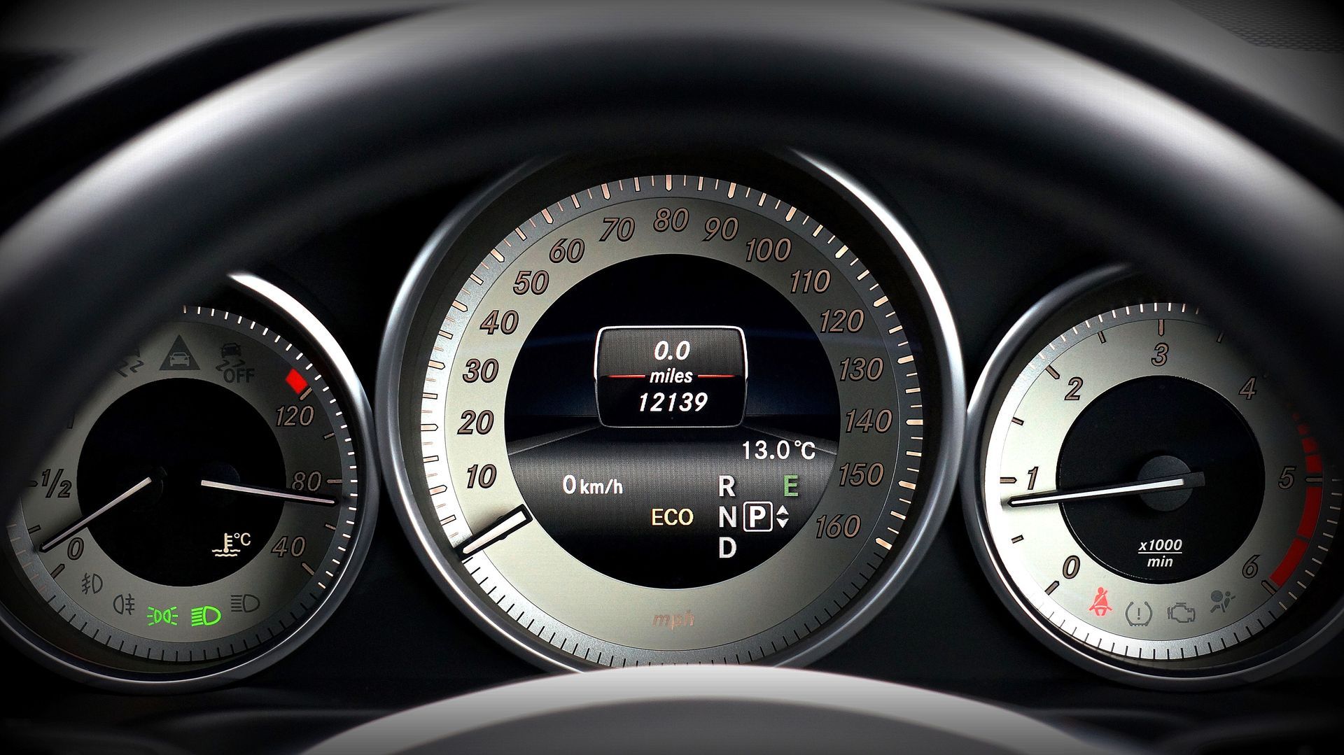 Car dashboard instrument cluster with speedometer, tachometer, fuel gauge, and digital display in a silver and black design