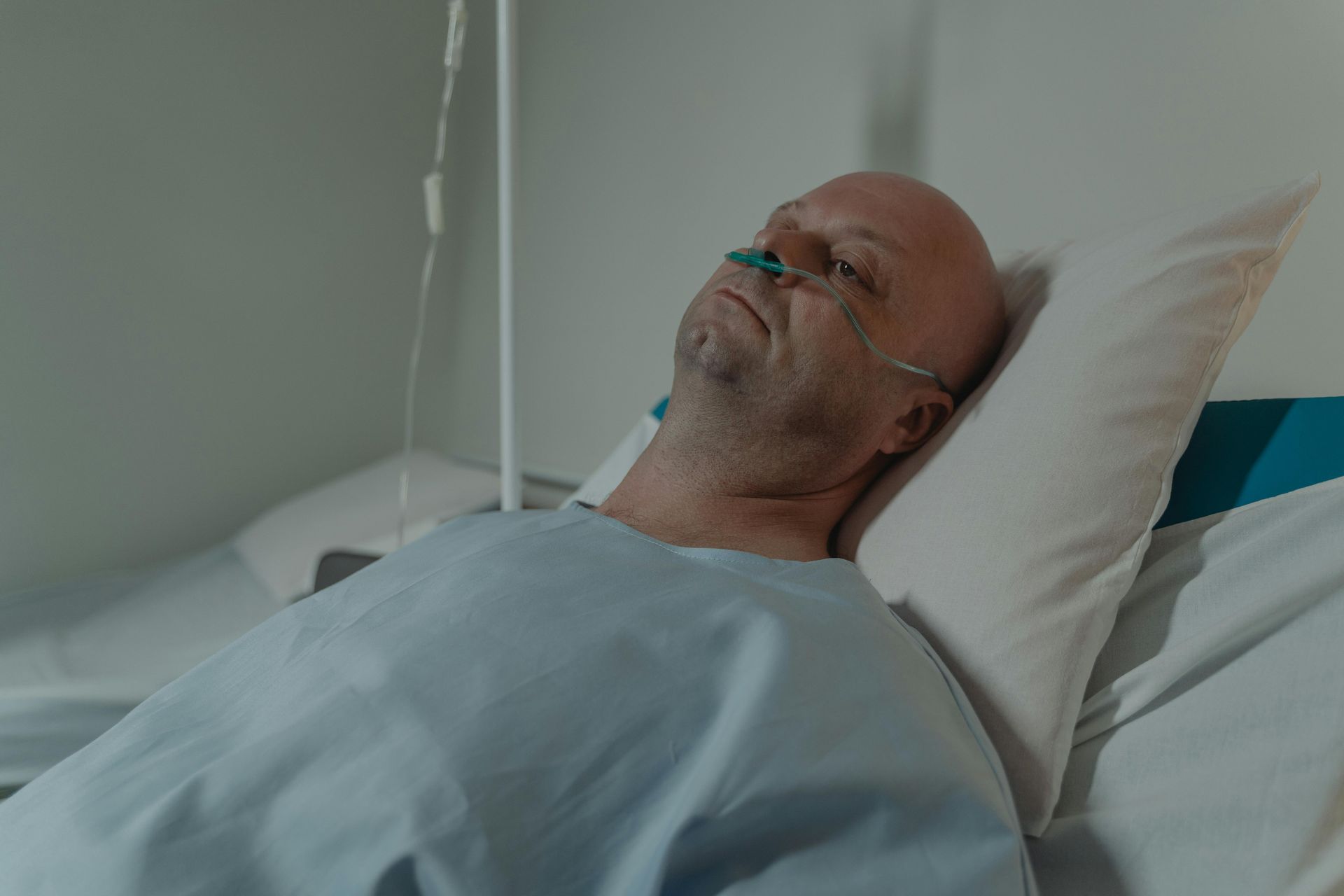 Man lying in a hospital bed with an oxygen tube, resting under a light blue blanket