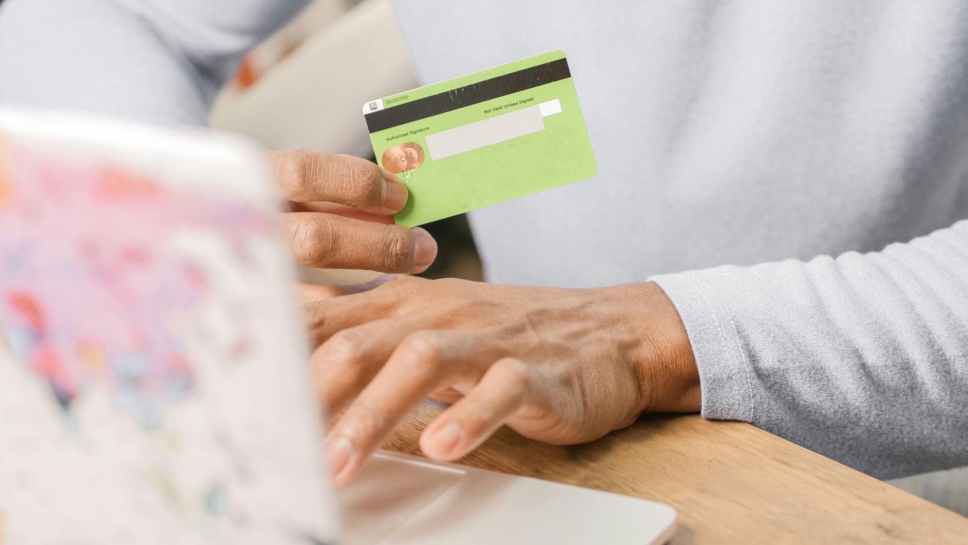 Hands using a green credit card to shop on a laptop keyboard