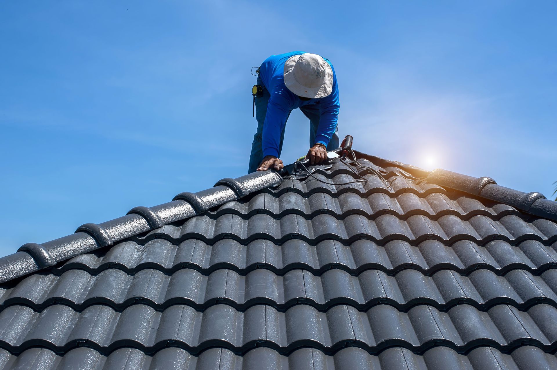 Roofer in Blue Workwear on a Dark Gray Tile Roof — C&A Roofing In Tamworth, NSW