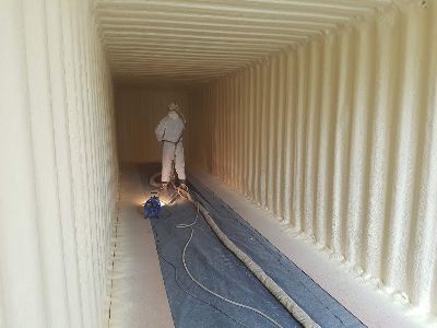 A man is spraying foam on the walls of a shipping container.