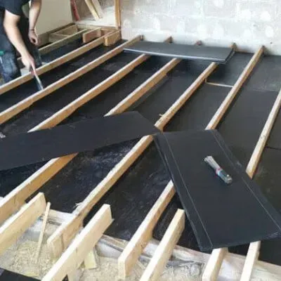 A man is laying black tiles on a wooden floor.