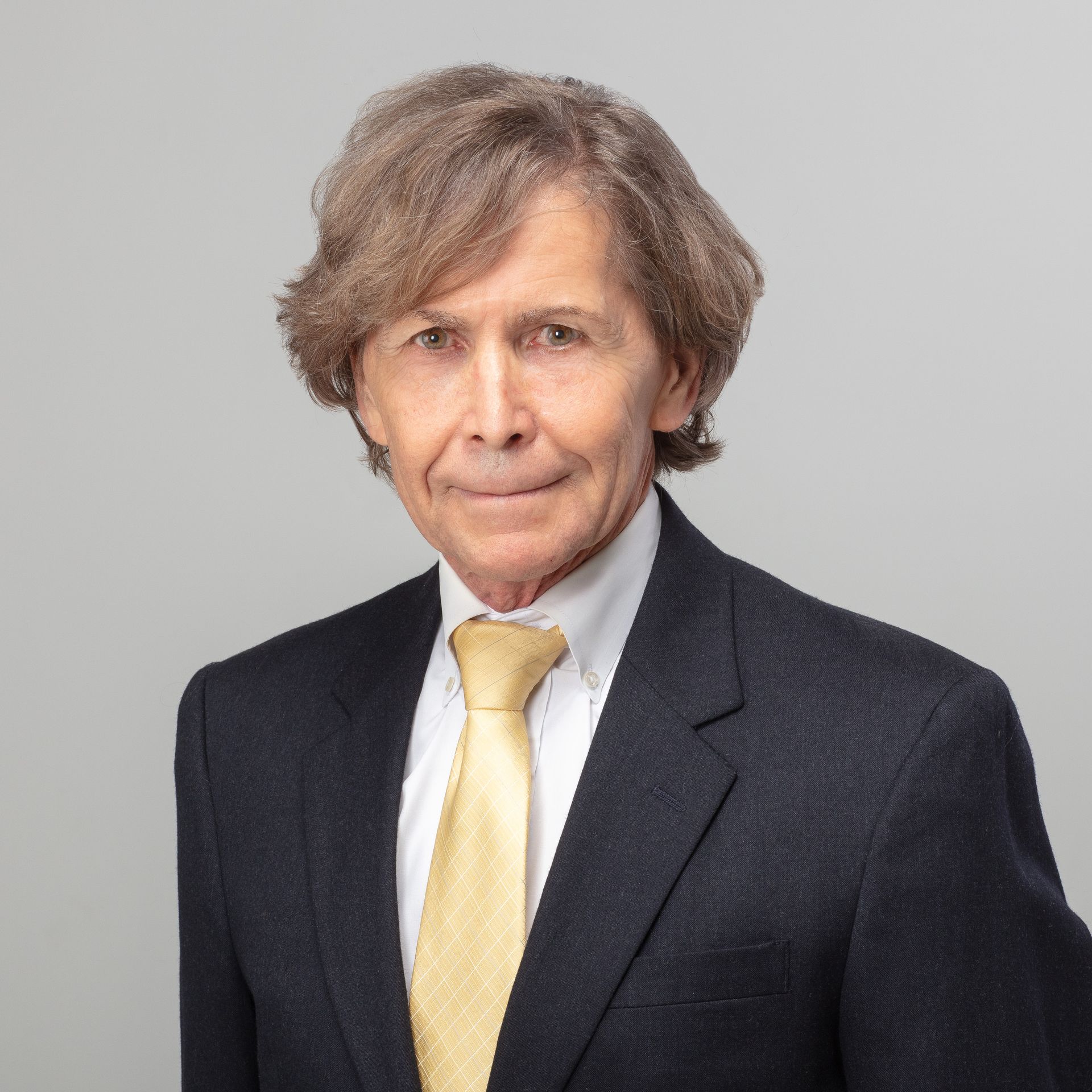 Man in suit, gold tie, looking at the camera against a gray background.