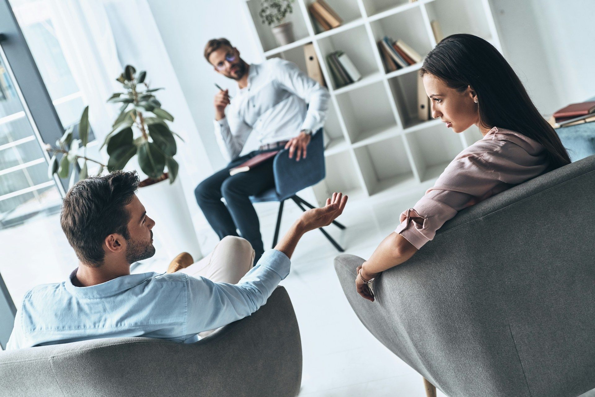 Couple in therapy, conversing with a therapist in a modern office setting.