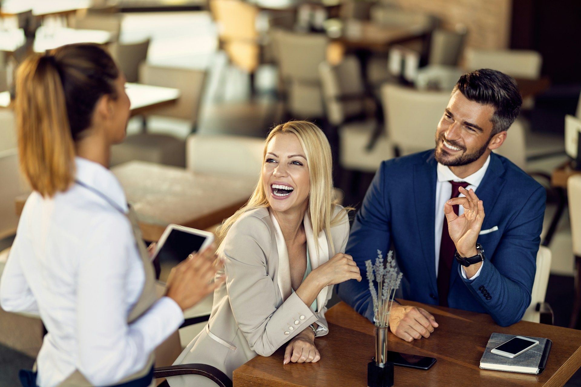 A server talking to a couple smiling and laughing at a table in a restaurant.