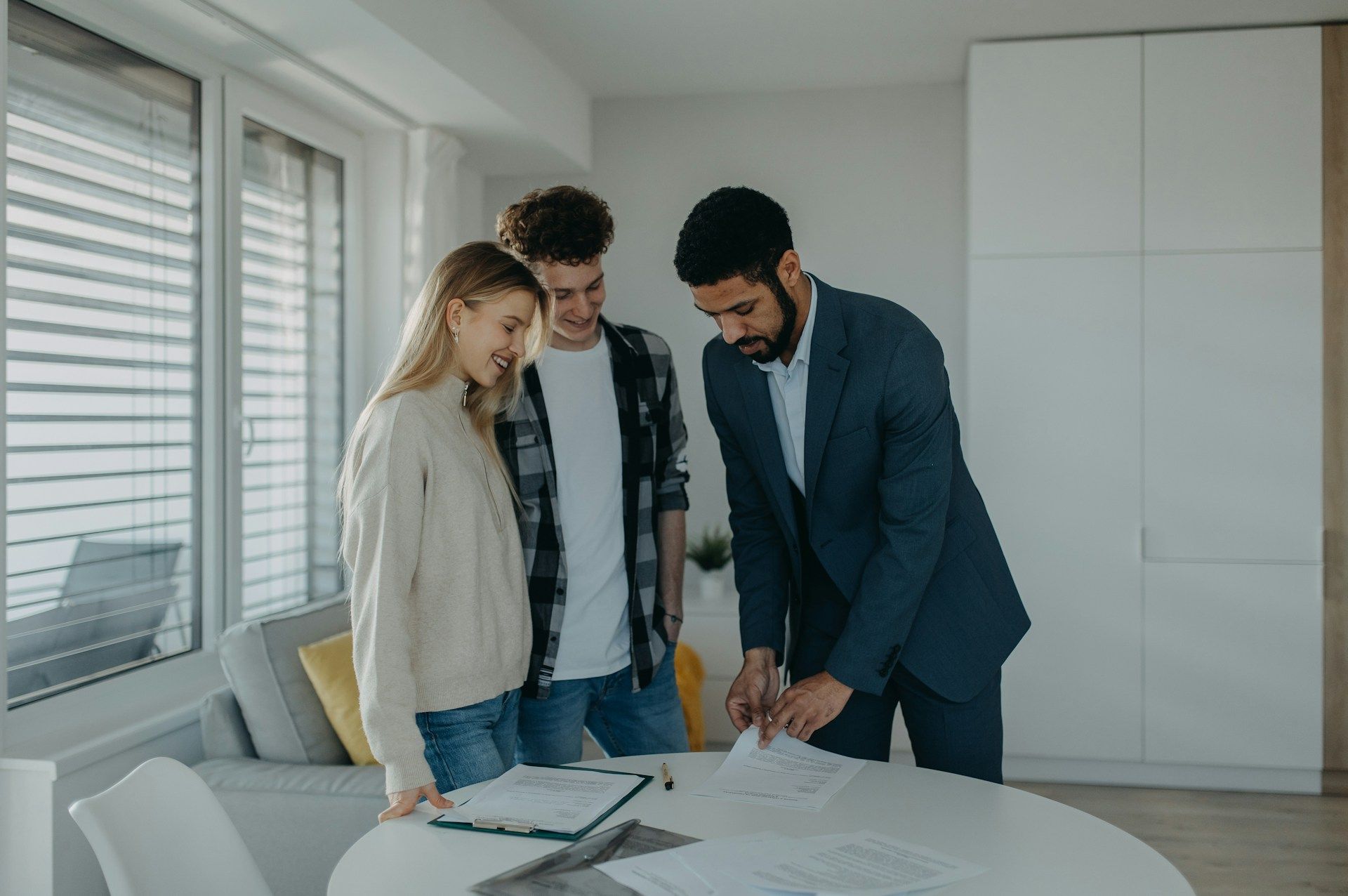 Real estate agent reviews documents with a couple in a bright room.