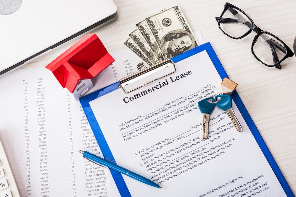 Commercial lease document with money, keys, and a model house on a desk.