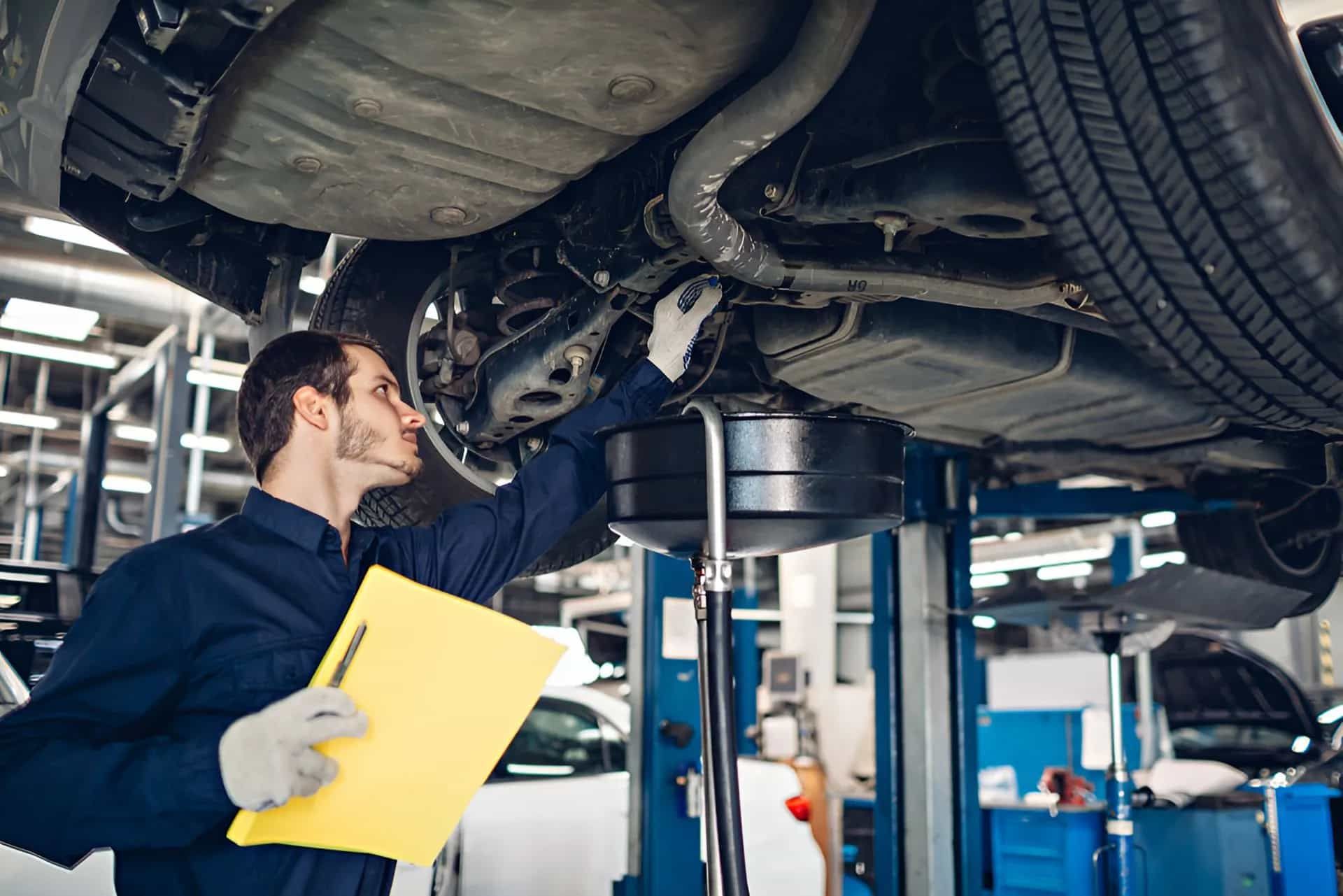 A Man Is Working On The Underside Of A Car In A Garage — Manning Smash & Auto Repairs In Wingham, NSW
