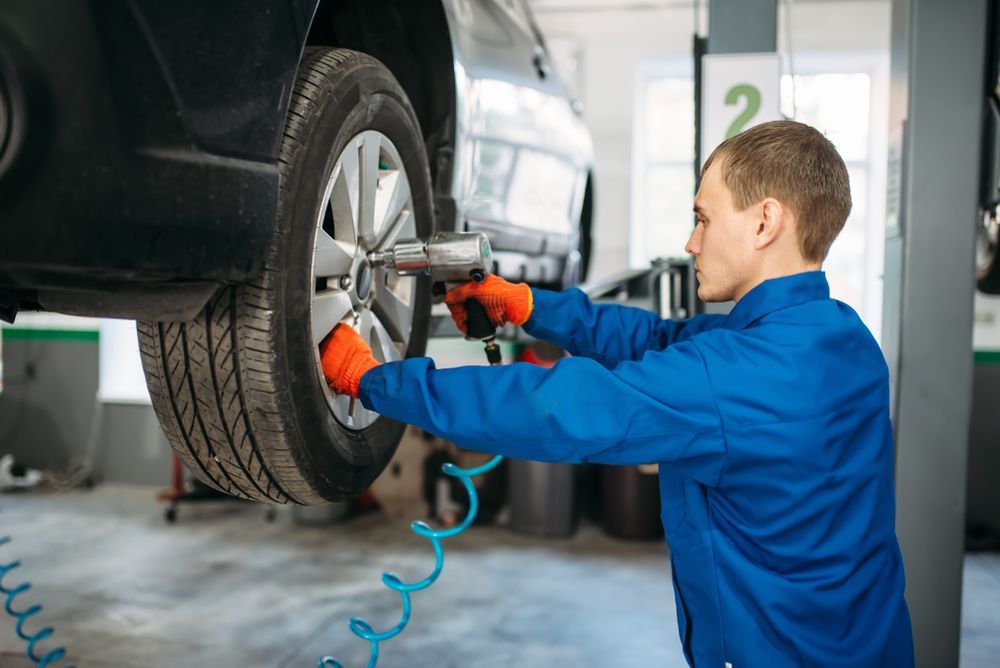 A Man Is Changing A Tyre On A Car In A Garage — Manning Smash & Auto Repairs In Wingham, NSW