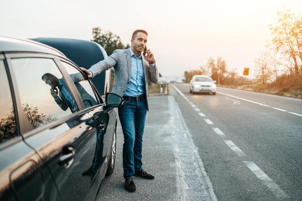 A Man Is Standing Next To A Broken Down Car Talking On A Cell Phone — Manning Smash & Auto Repairs In Forster, NSW