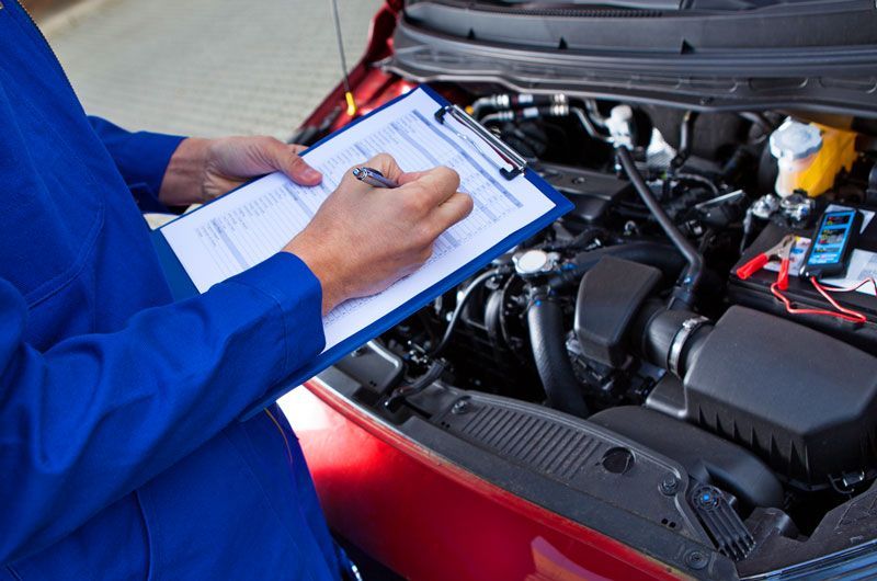 A Mechanic Is Writing On A Clipboard While Looking Under The Hood Of A Car — Manning Smash & Auto Repairs In Wingham, NSW