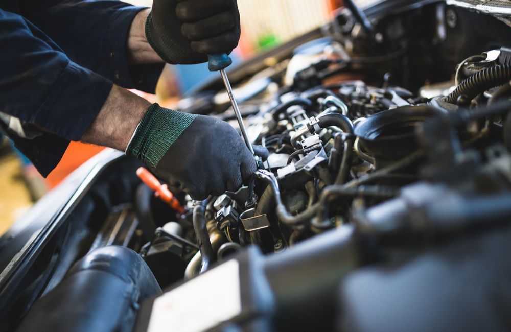 A Man Is Working On A Car Engine With A Screwdriver — Manning Smash & Auto Repairs In Wingham, NSW