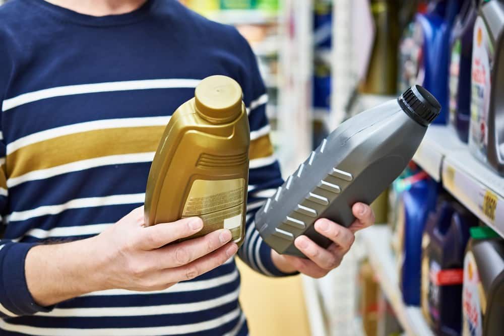 A Man Is Holding Two Bottles Of Oil In His Hands In A Store — Manning Smash & Auto Repairs In Wingham, NSW