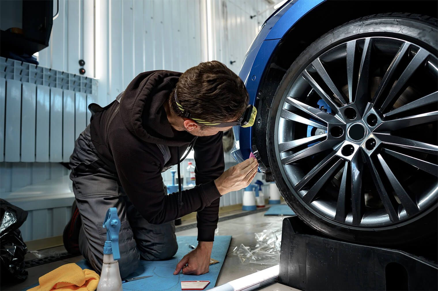 A Man Is Kneeling Down Next To A Blue Car In A Garage — Manning Smash & Auto Repairs In Wingham, NSW