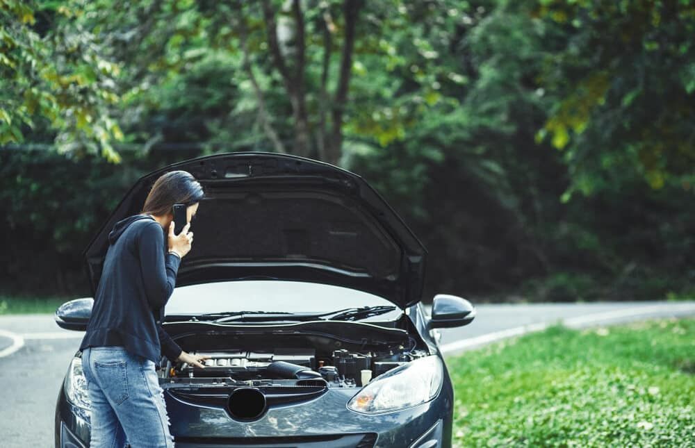 A Woman Is Standing Next To A Broken Down Car Talking On A Cell Phone — Manning Smash & Auto Repairs In Forster, NSW
