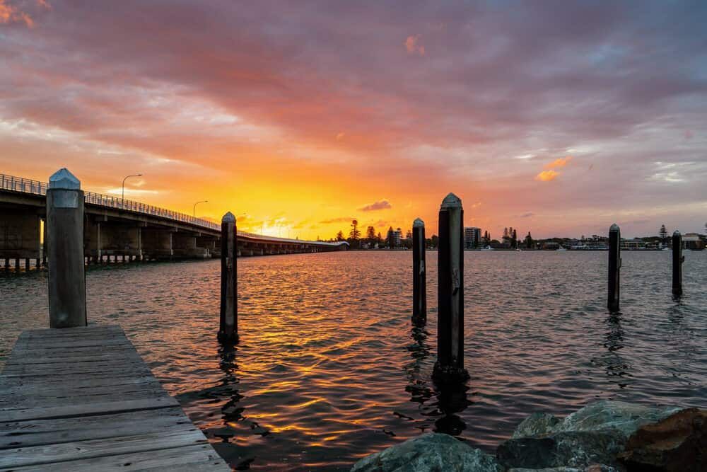 A Dock Overlooking A Body Of Water With A Bridge In The Background At Sunset — Manning Smash & Auto Repairs In Forster, NSW