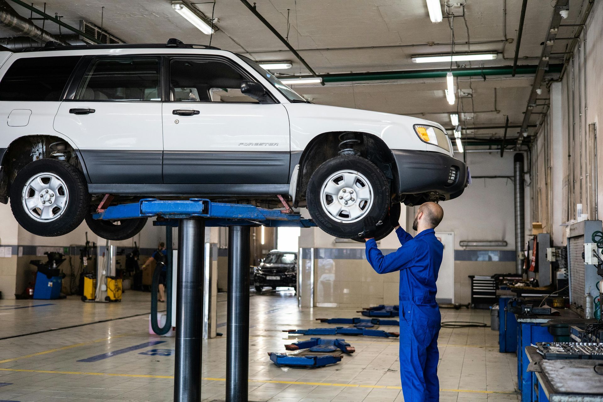 A Man Is Working On A Car On A Lift In A Garage - Manning Smash & Auto Repairs In Forster, NSW