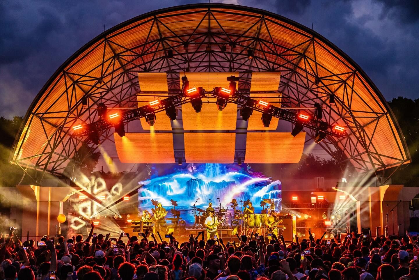 A large crowd of people are watching a band on stage at a concert.