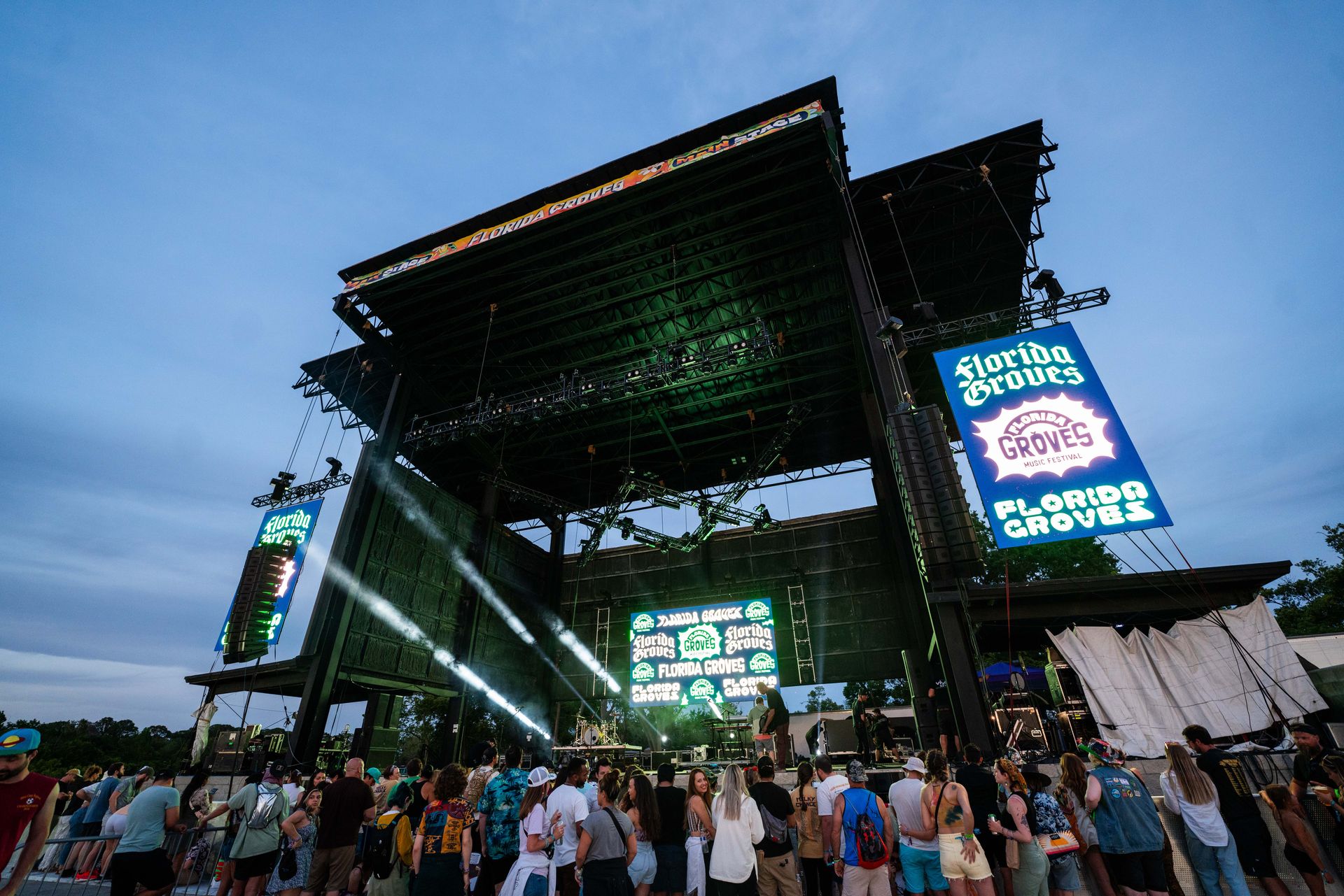 A crowd of people are standing in front of a large stage at a music festival.