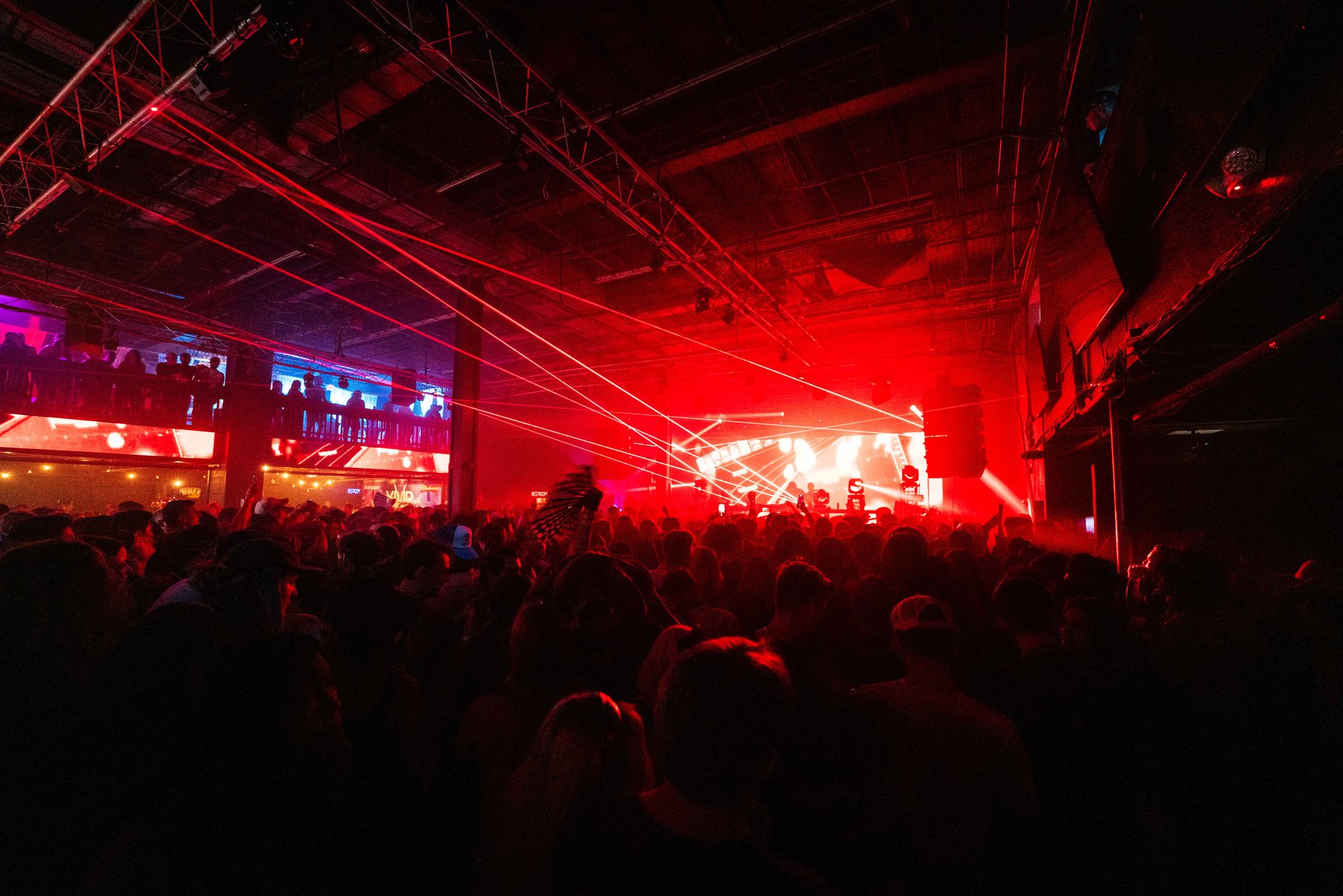 A crowd of people are watching a concert in a dark room with red lights.