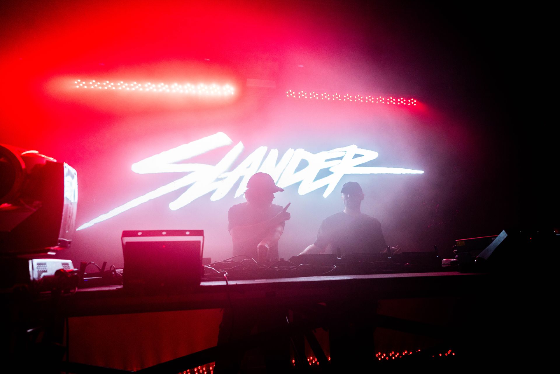 A couple of people standing in front of a stage with a red light behind them.