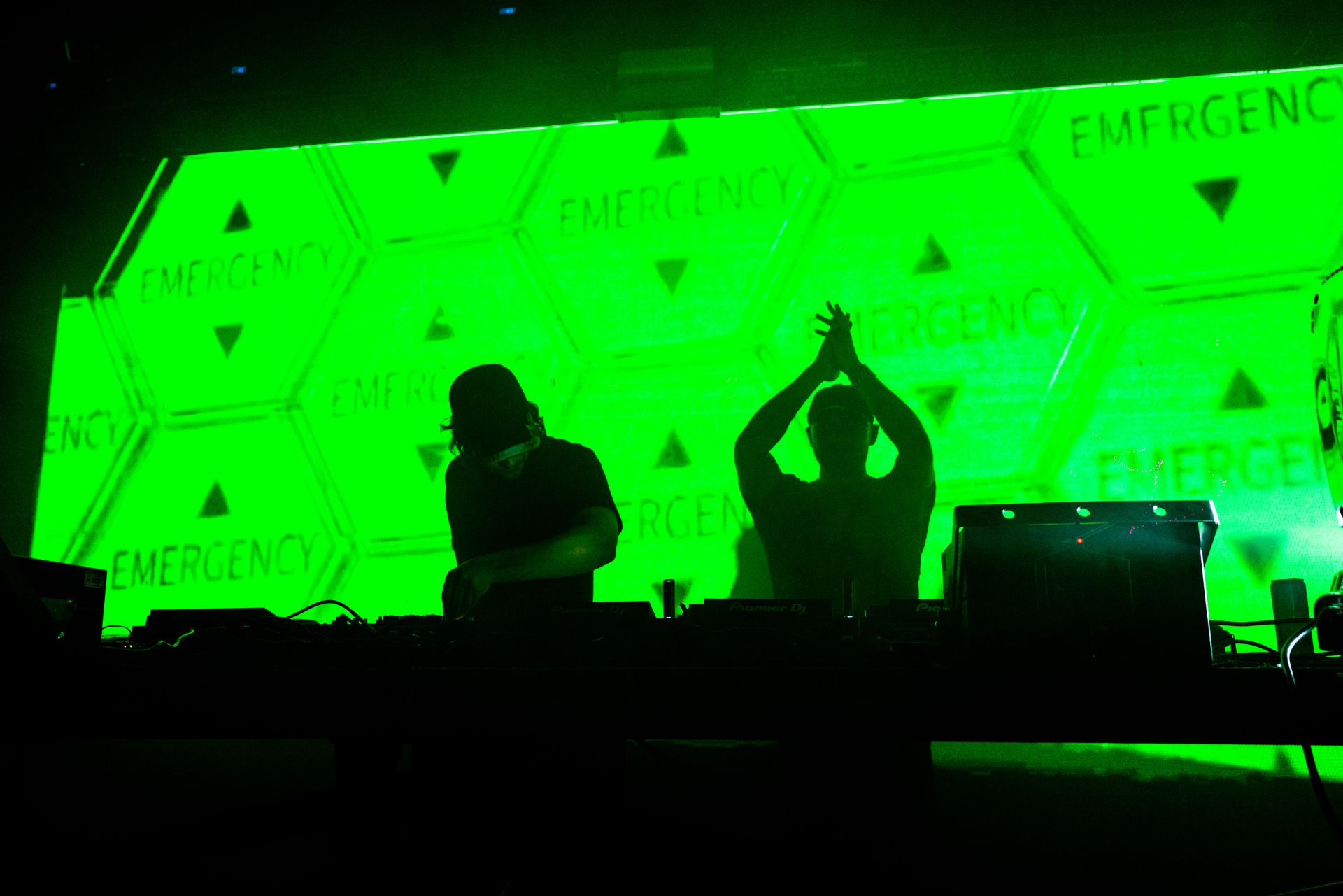 Two people are standing in front of a green screen that says emergency