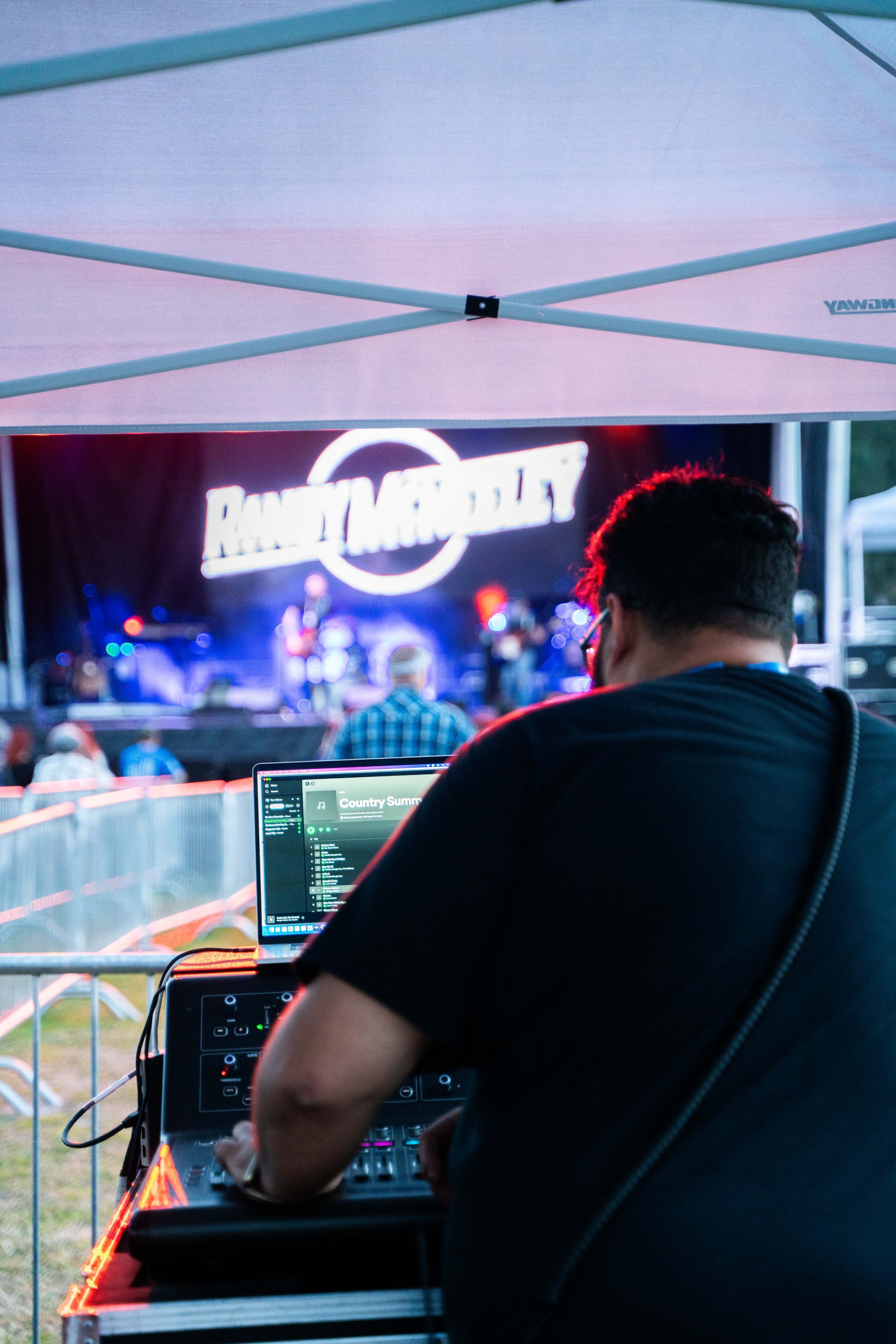 A man is playing music on a laptop in front of a stage.