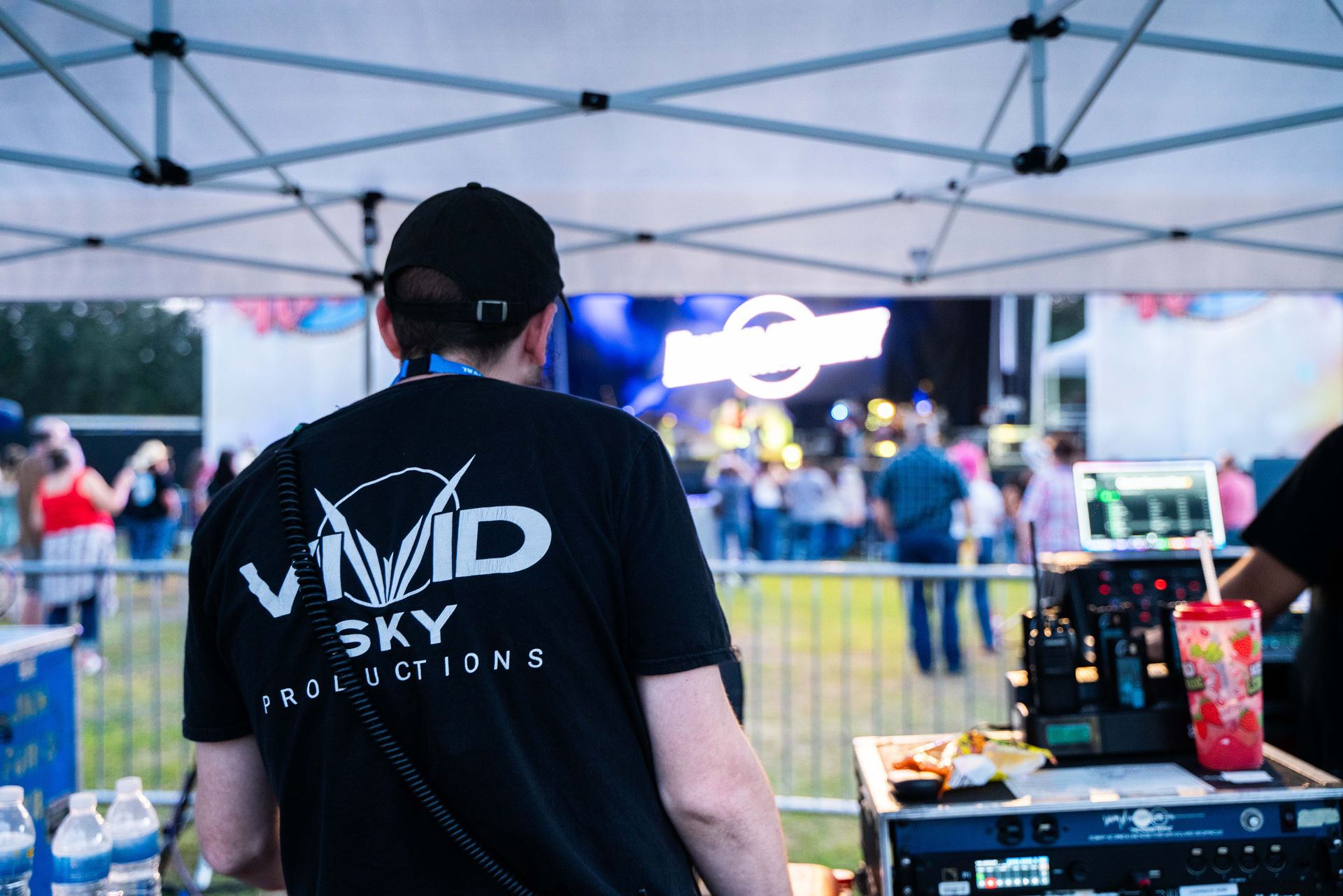 A man wearing a vivid sky t-shirt is standing in front of a stage.