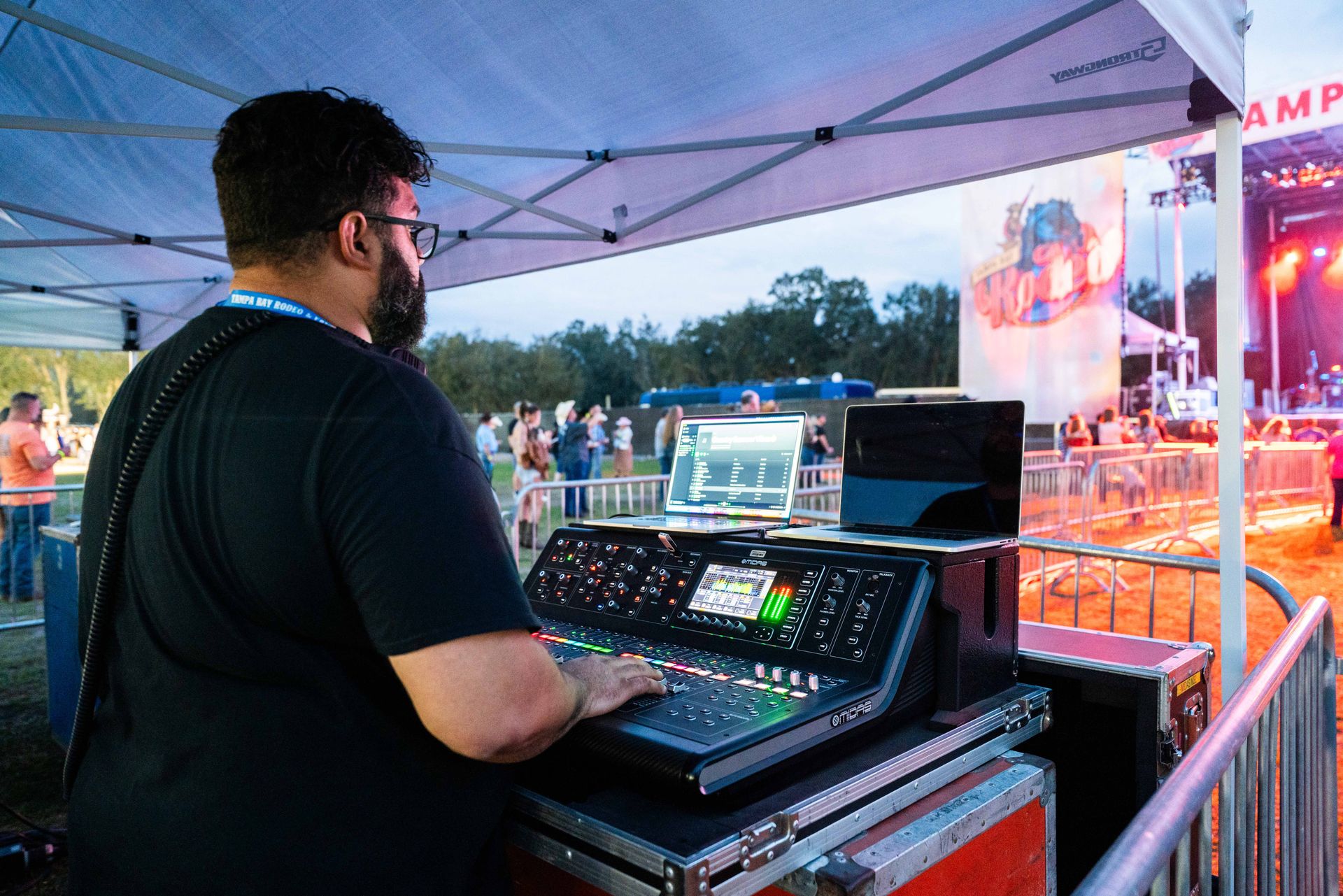 A man is standing in front of a mixer at a concert.