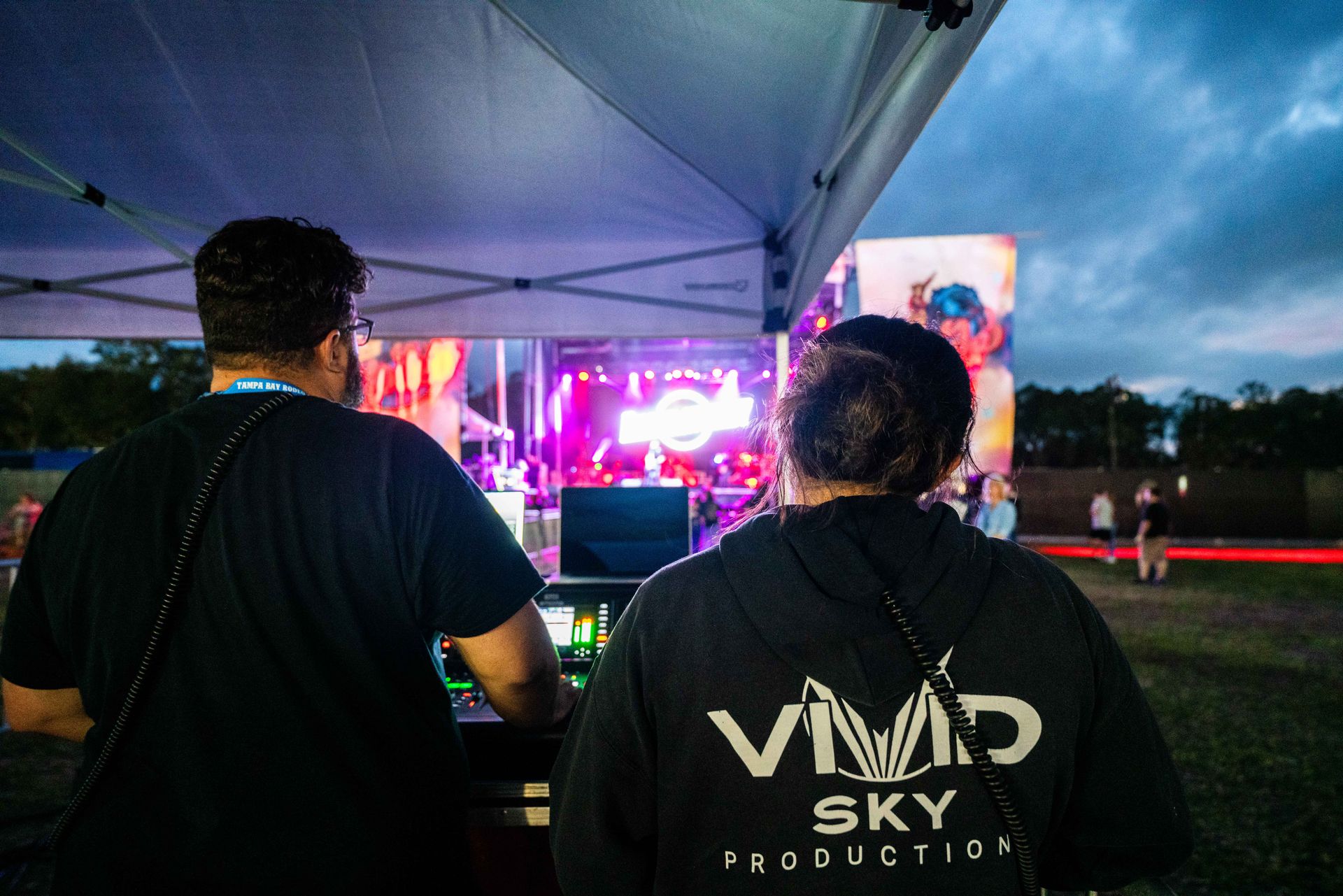 A man and a woman are standing under a tent watching a concert.