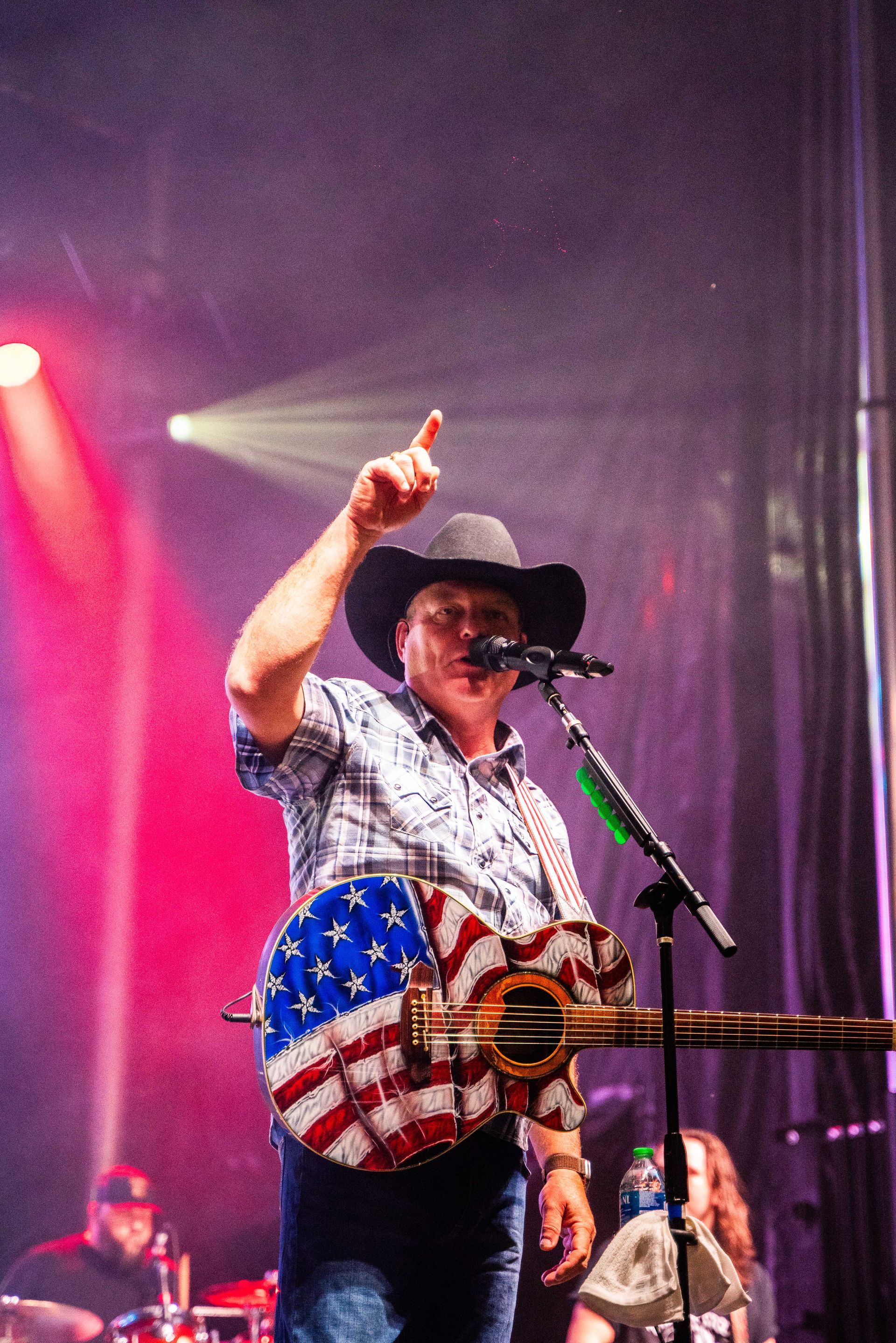 A man in a cowboy hat is playing a guitar and singing into a microphone on a stage.