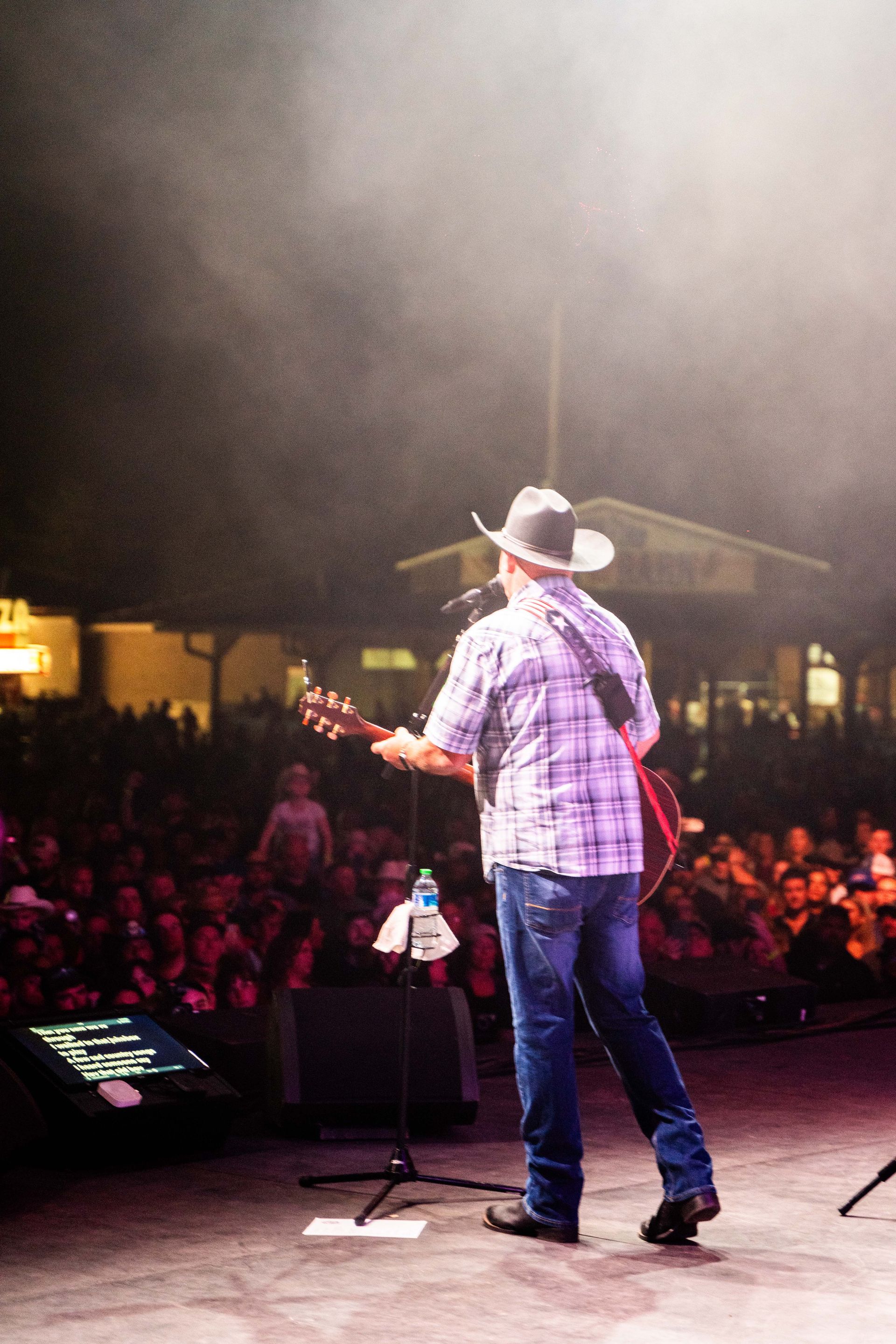 A man in a cowboy hat is playing a guitar on stage