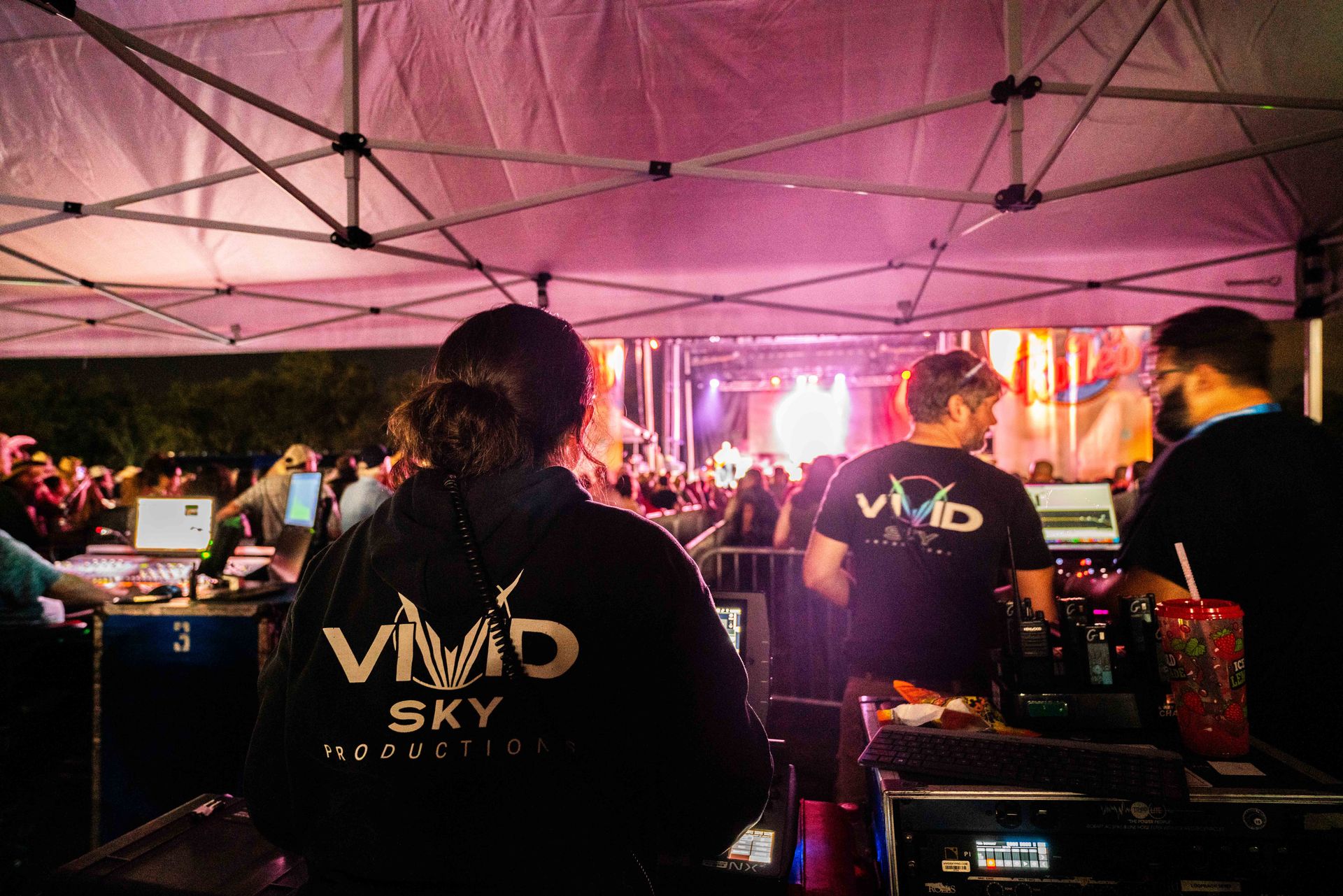 A woman wearing a vivid sky sweatshirt stands in front of a crowd at a concert.