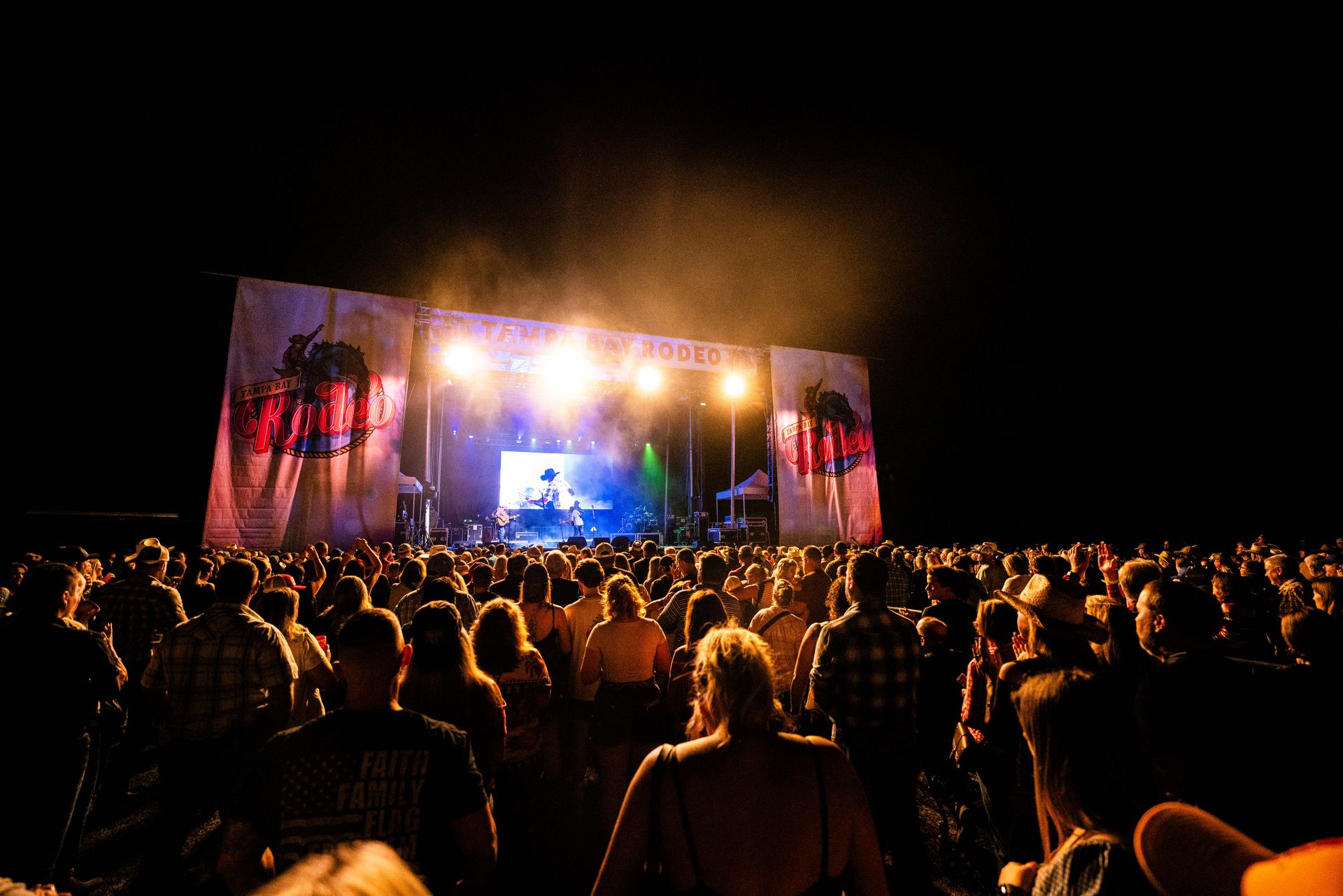 A crowd of people are sitting in front of a stage at a concert.
