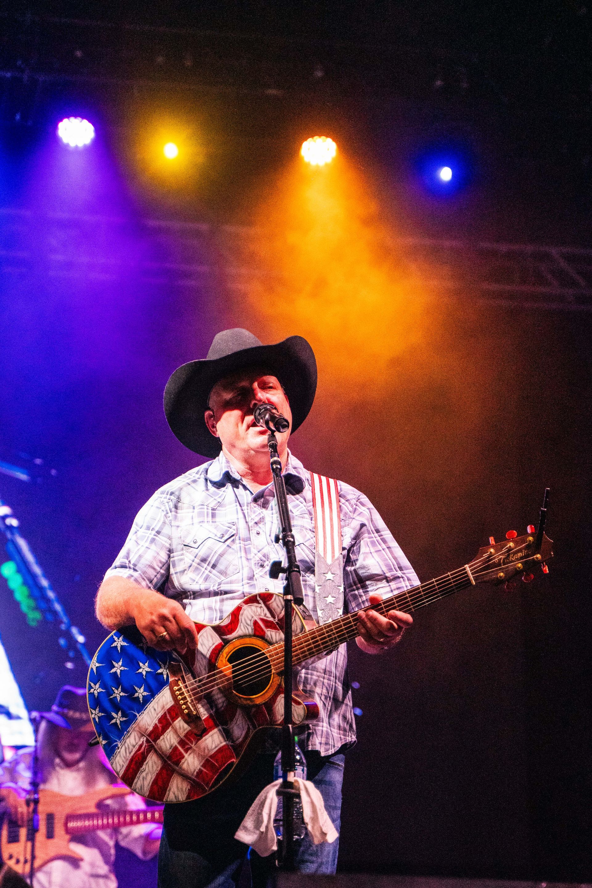 A man in a cowboy hat is playing a guitar and singing into a microphone on a stage.