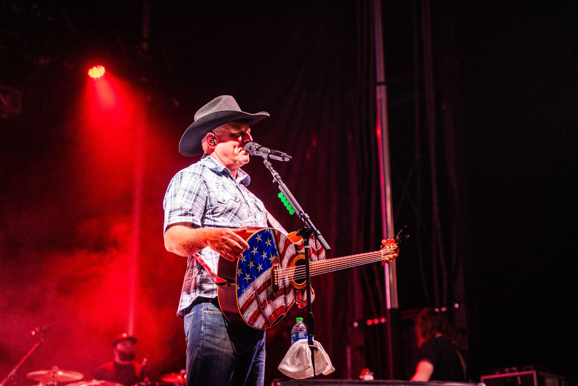 A man in a cowboy hat is playing a guitar and singing into a microphone on a stage.