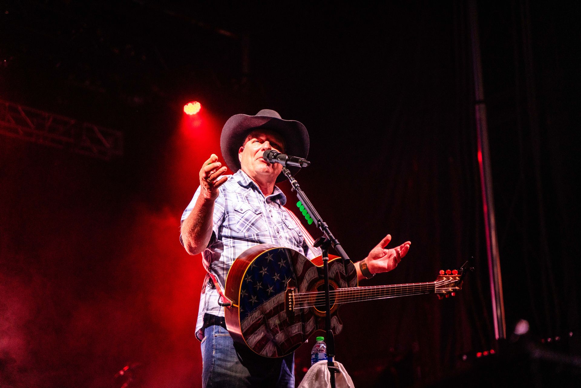 A man in a cowboy hat is playing a guitar and singing into a microphone on a stage.