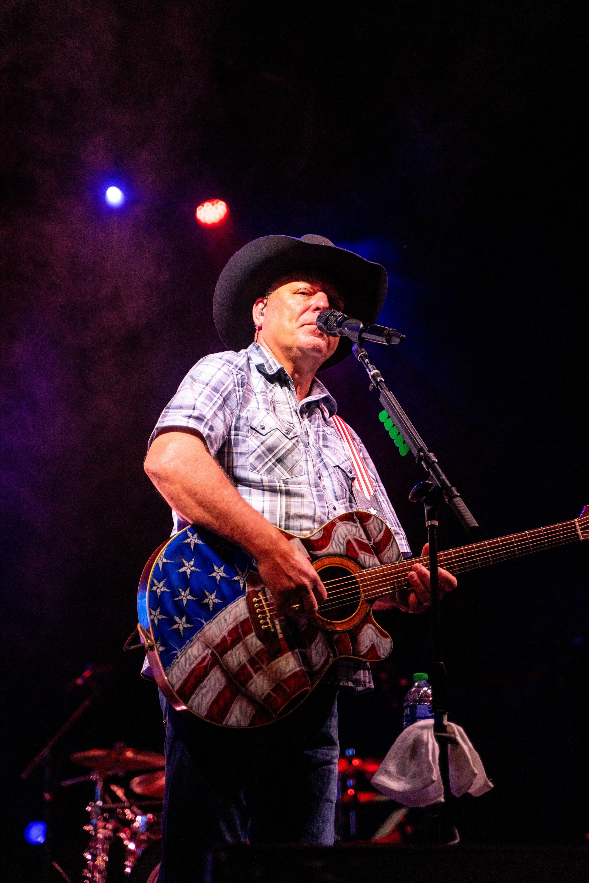 A man in a cowboy hat is playing a guitar and singing into a microphone.