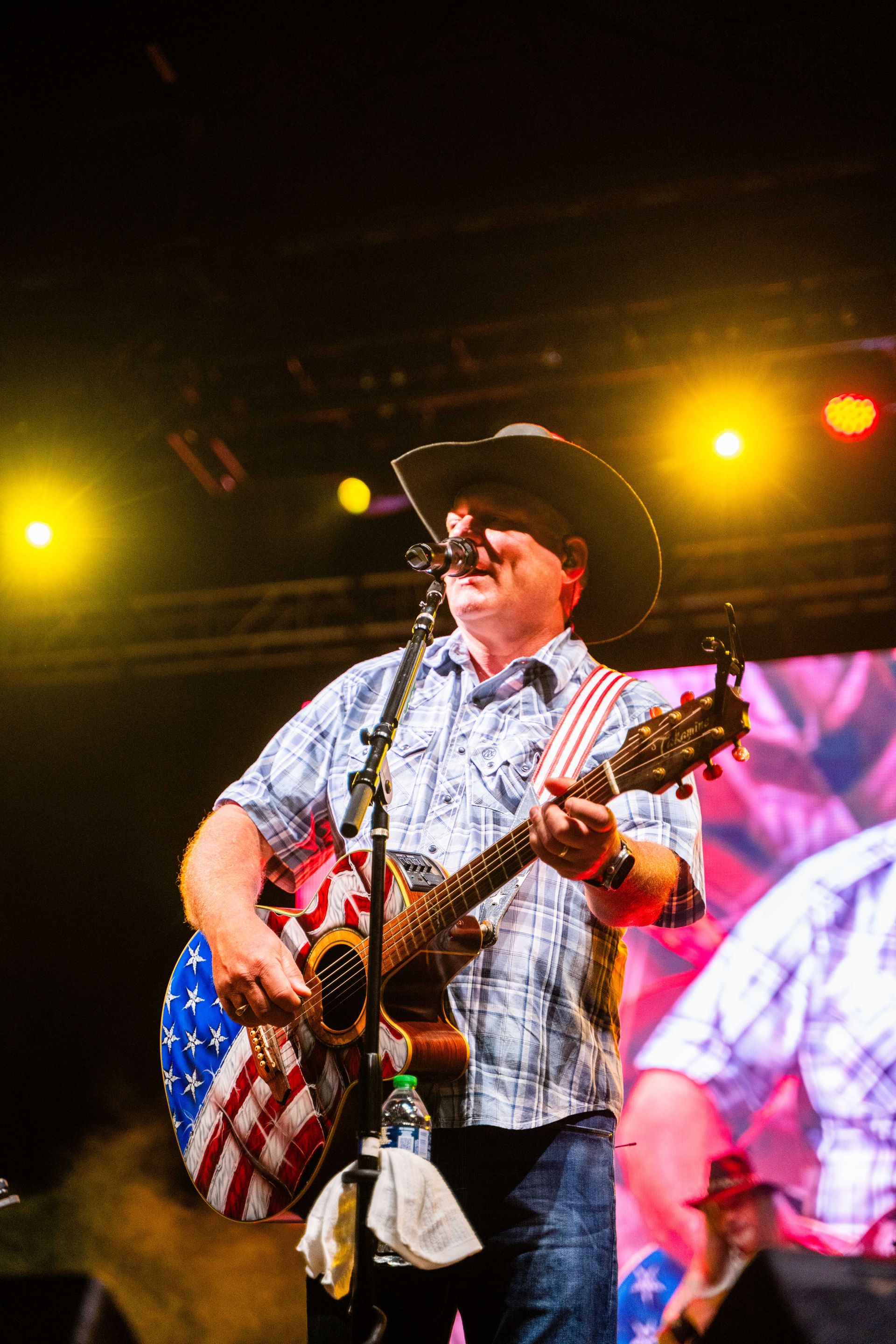 A man in a cowboy hat is playing a guitar and singing into a microphone on a stage.