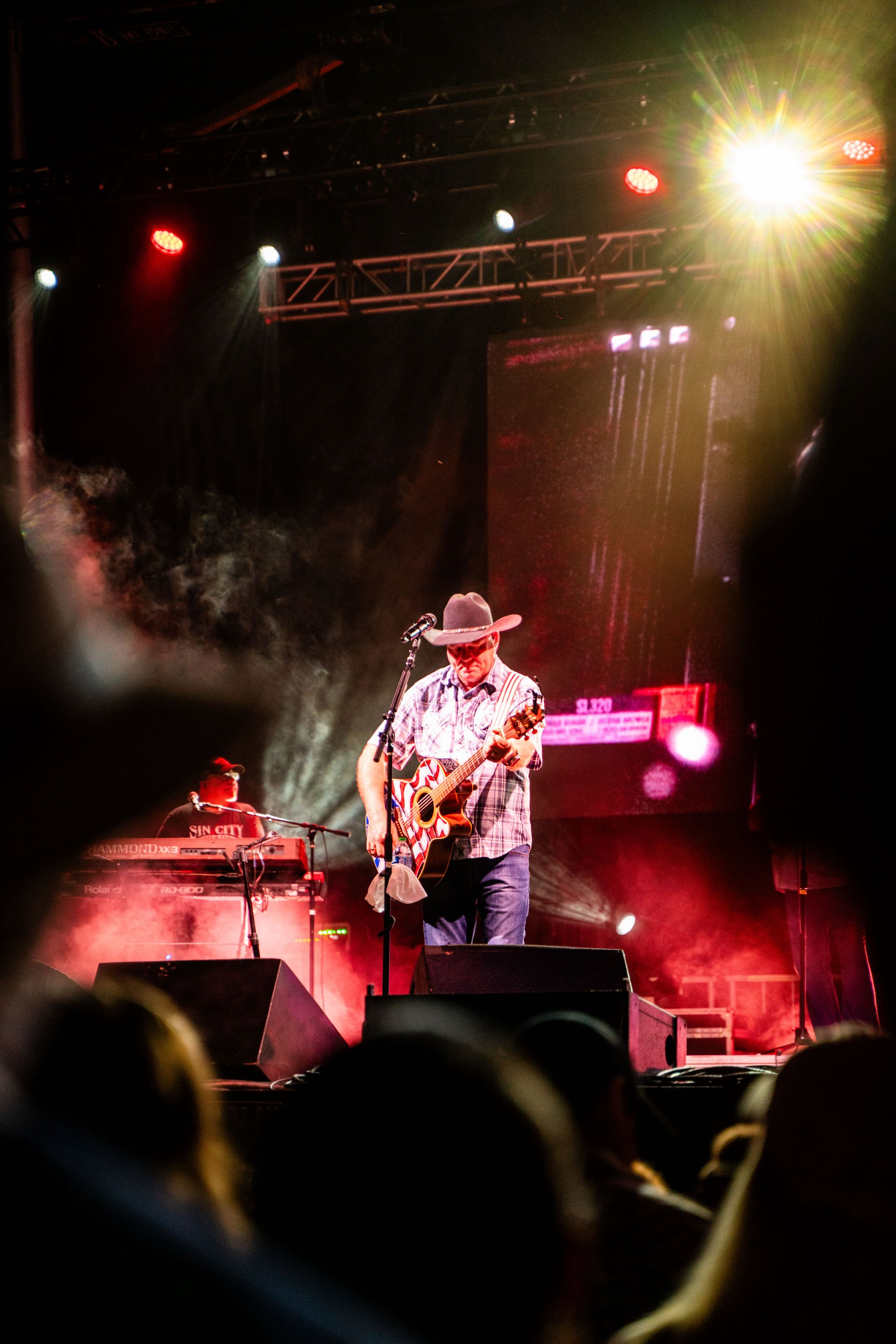 A man in a cowboy hat is playing a guitar on a stage in front of a crowd.