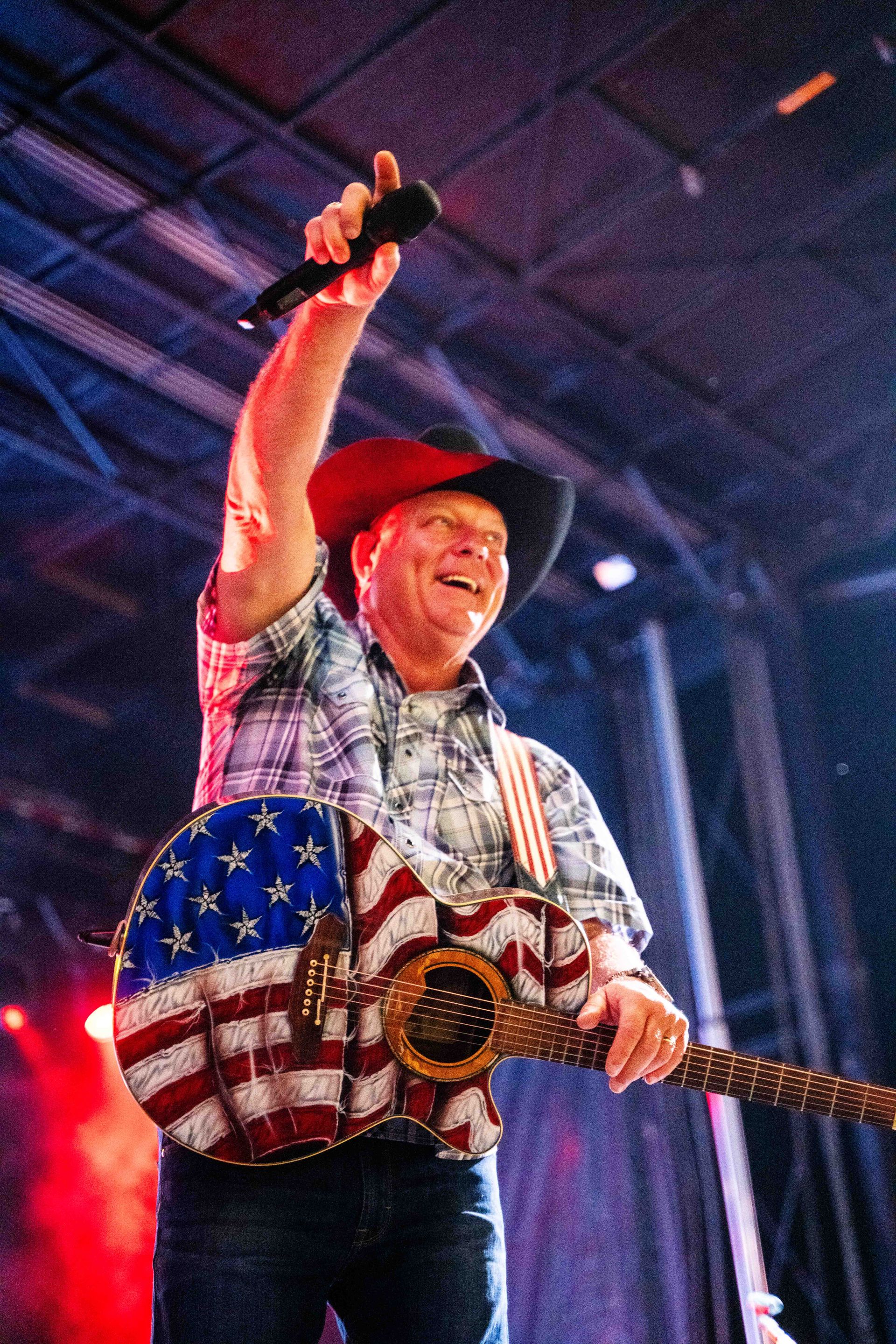 A man in a cowboy hat is playing a guitar and singing into a microphone.