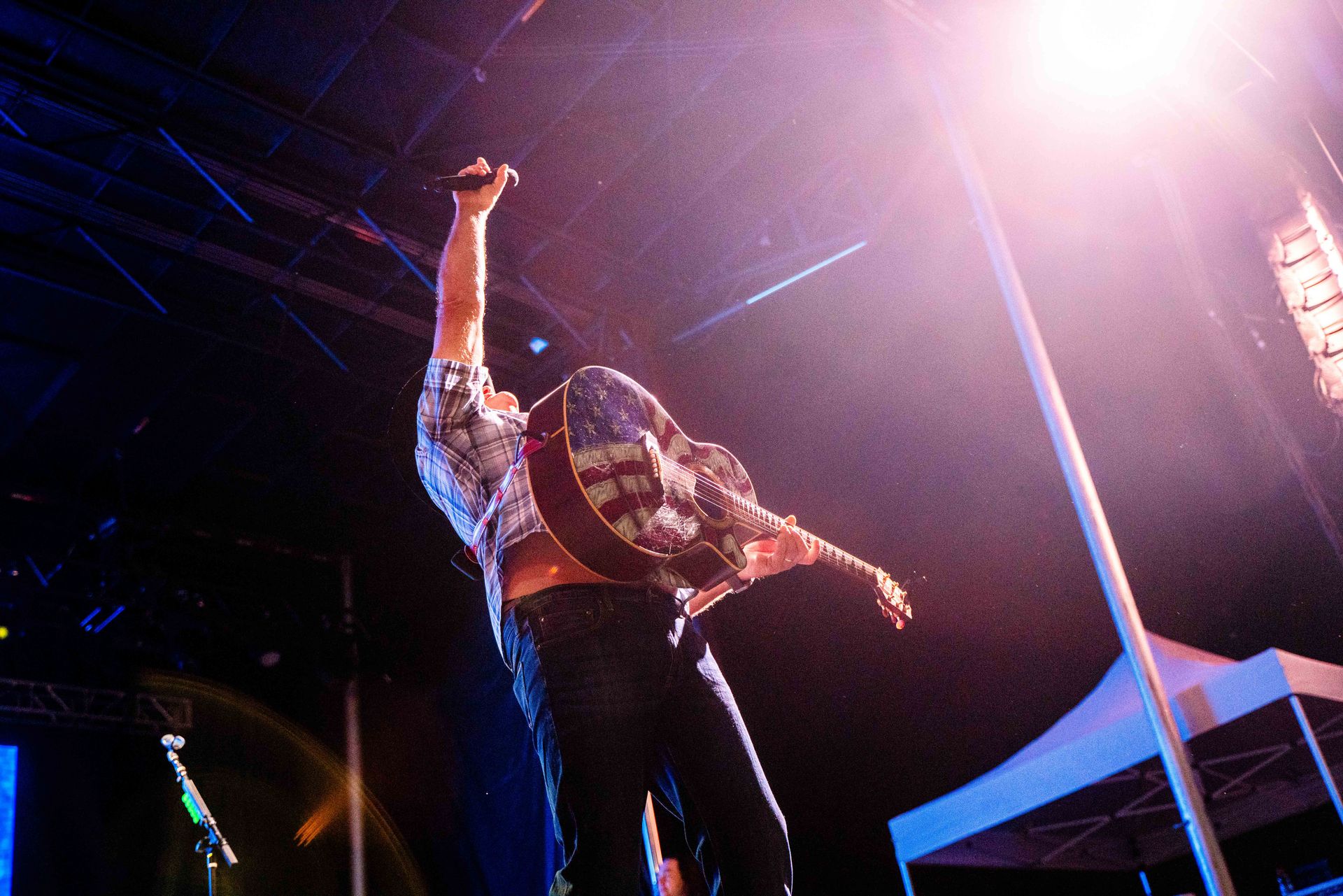 A man is singing into a microphone on a stage while holding a guitar.