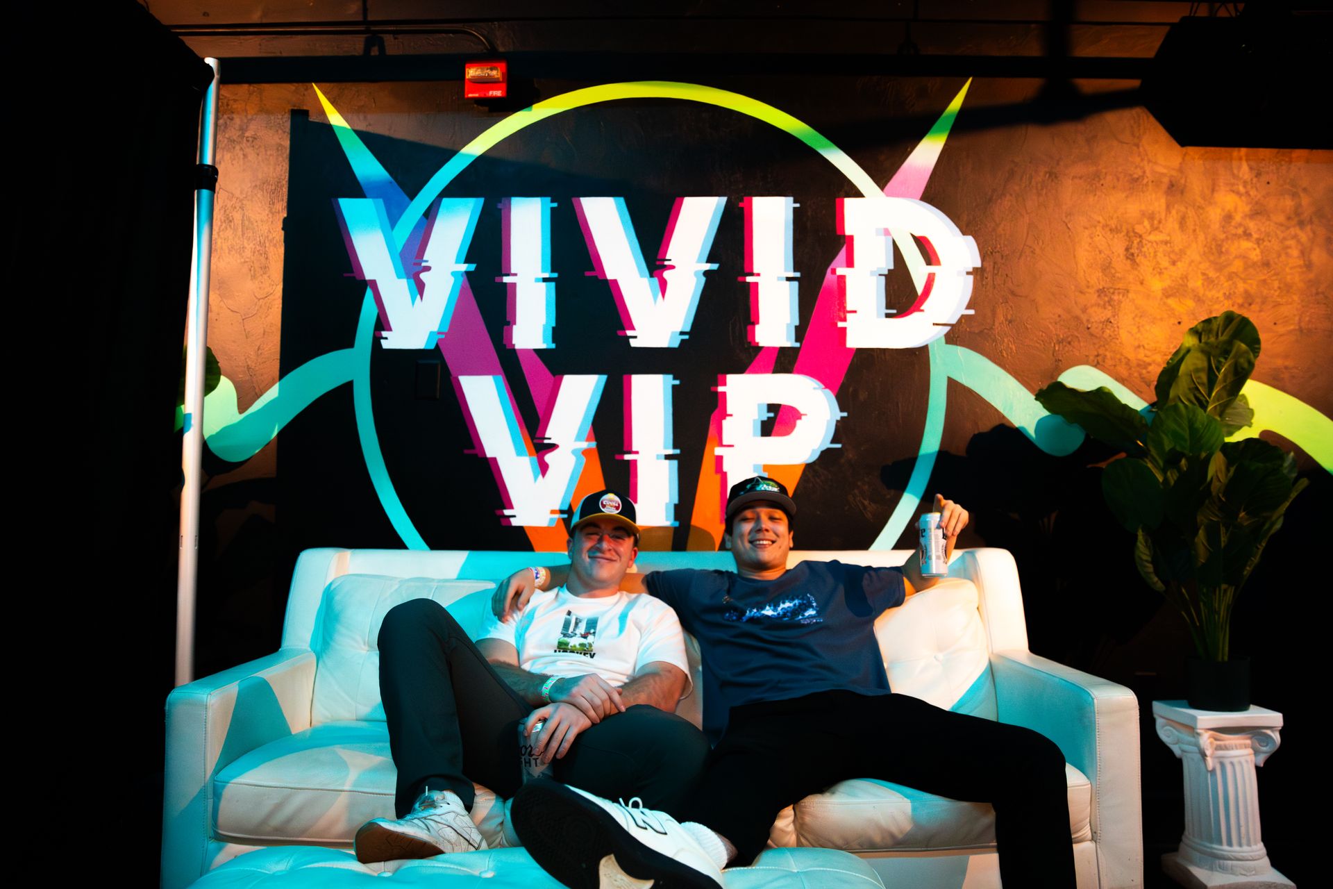 Two men are sitting on a couch in front of a sign that says vivid vip.