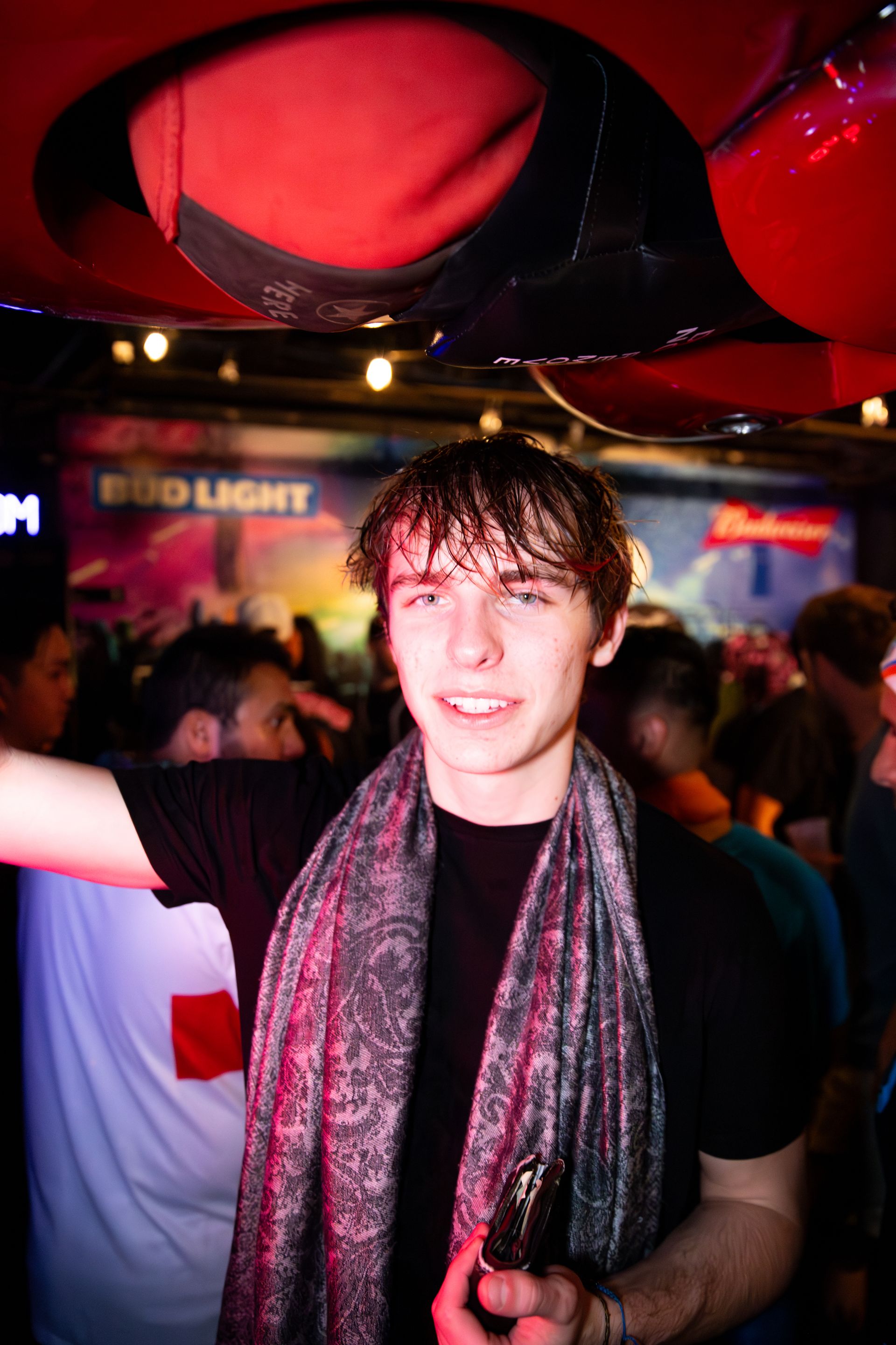 A young man is holding a bottle of beer in front of a bud light sign