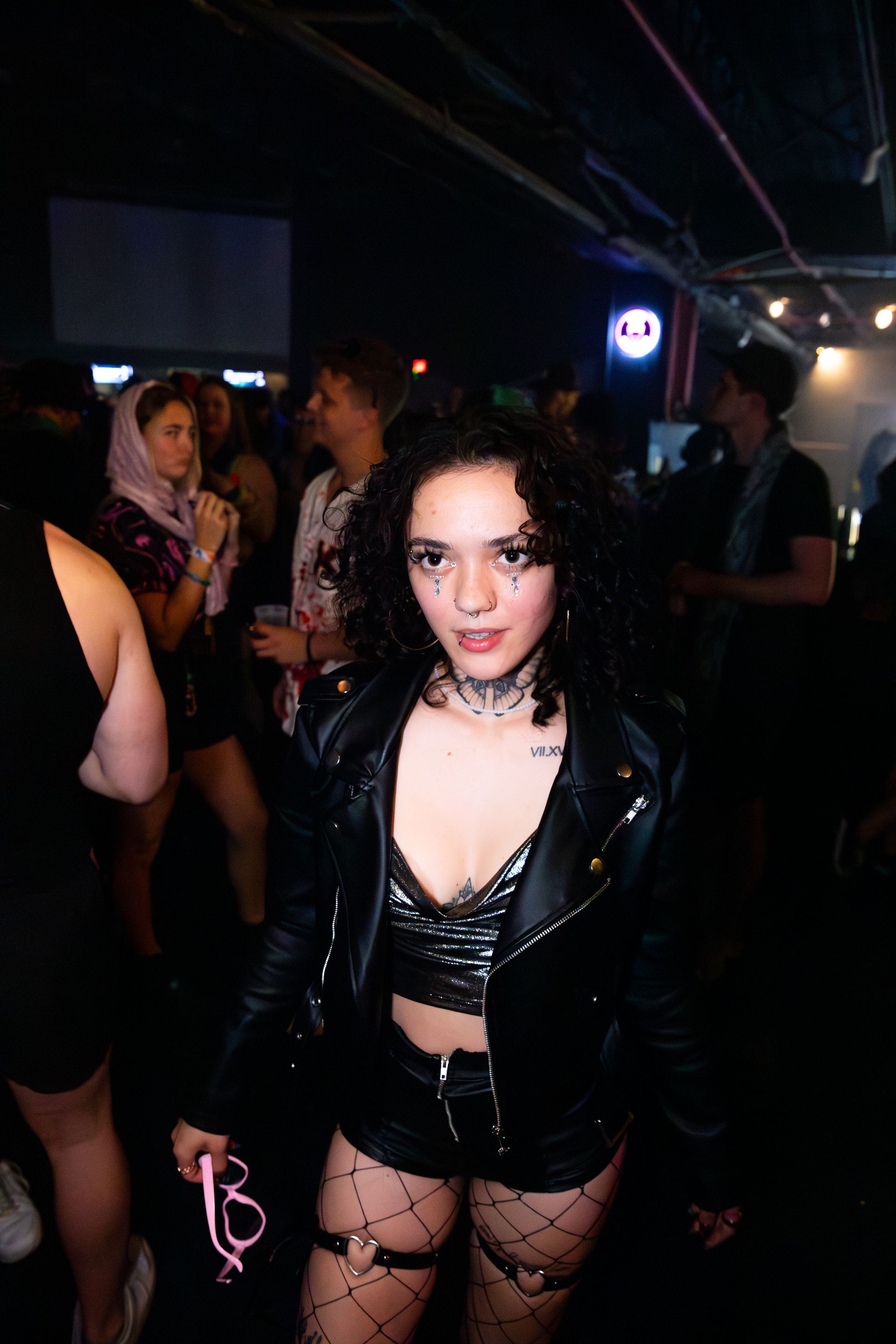 A woman in a leather jacket is standing in a crowd of people at a party.