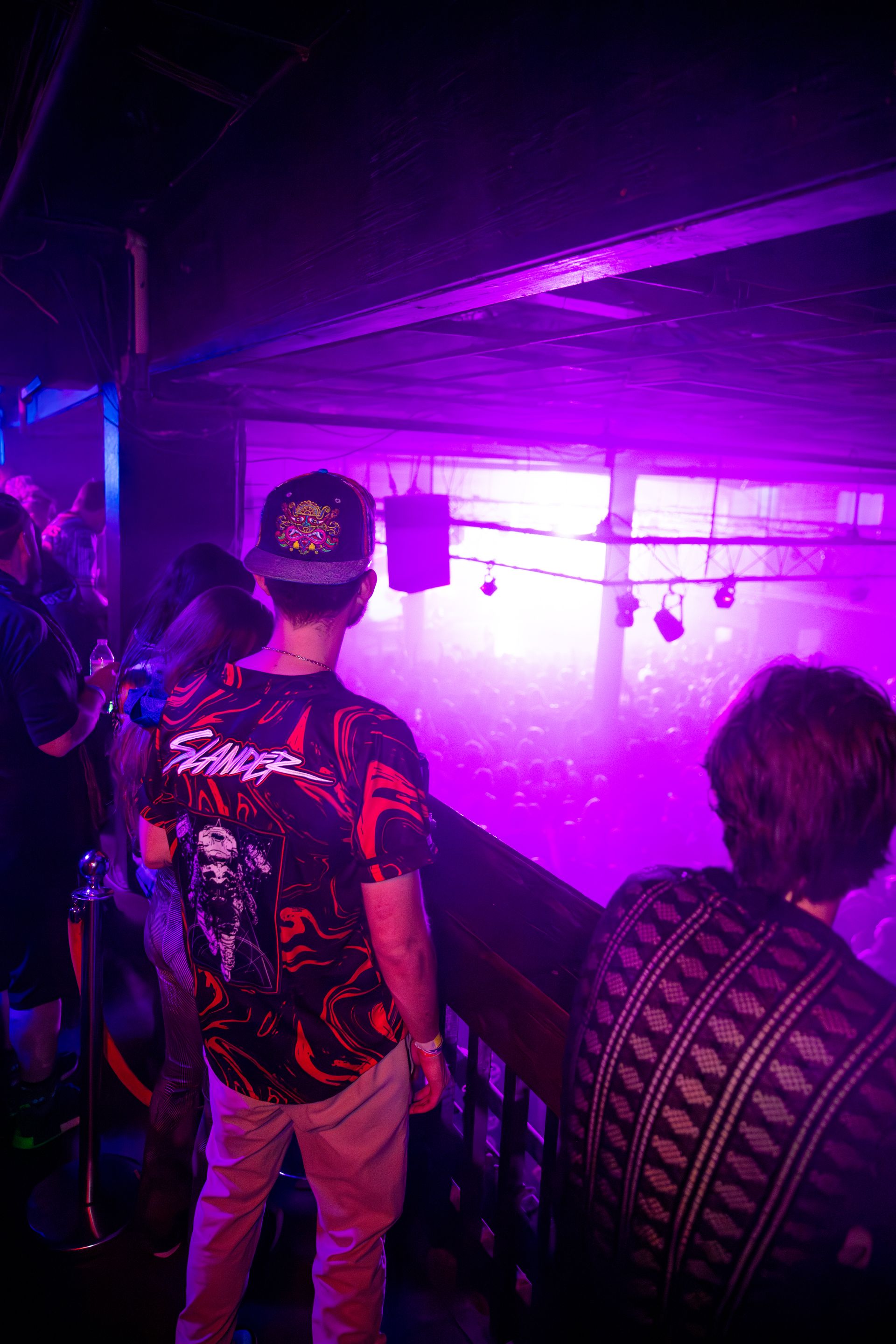A man in a ed hardy shirt is standing in a dark room with purple lights