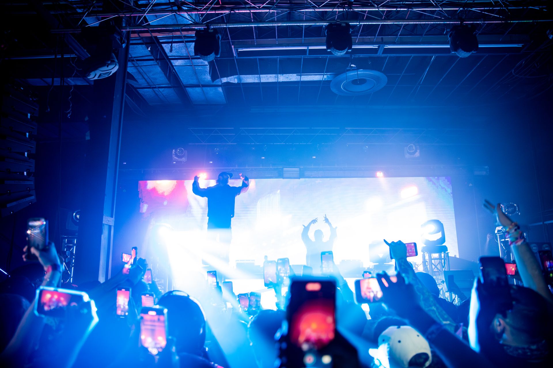 A crowd of people are taking pictures of a dj on stage at a concert.