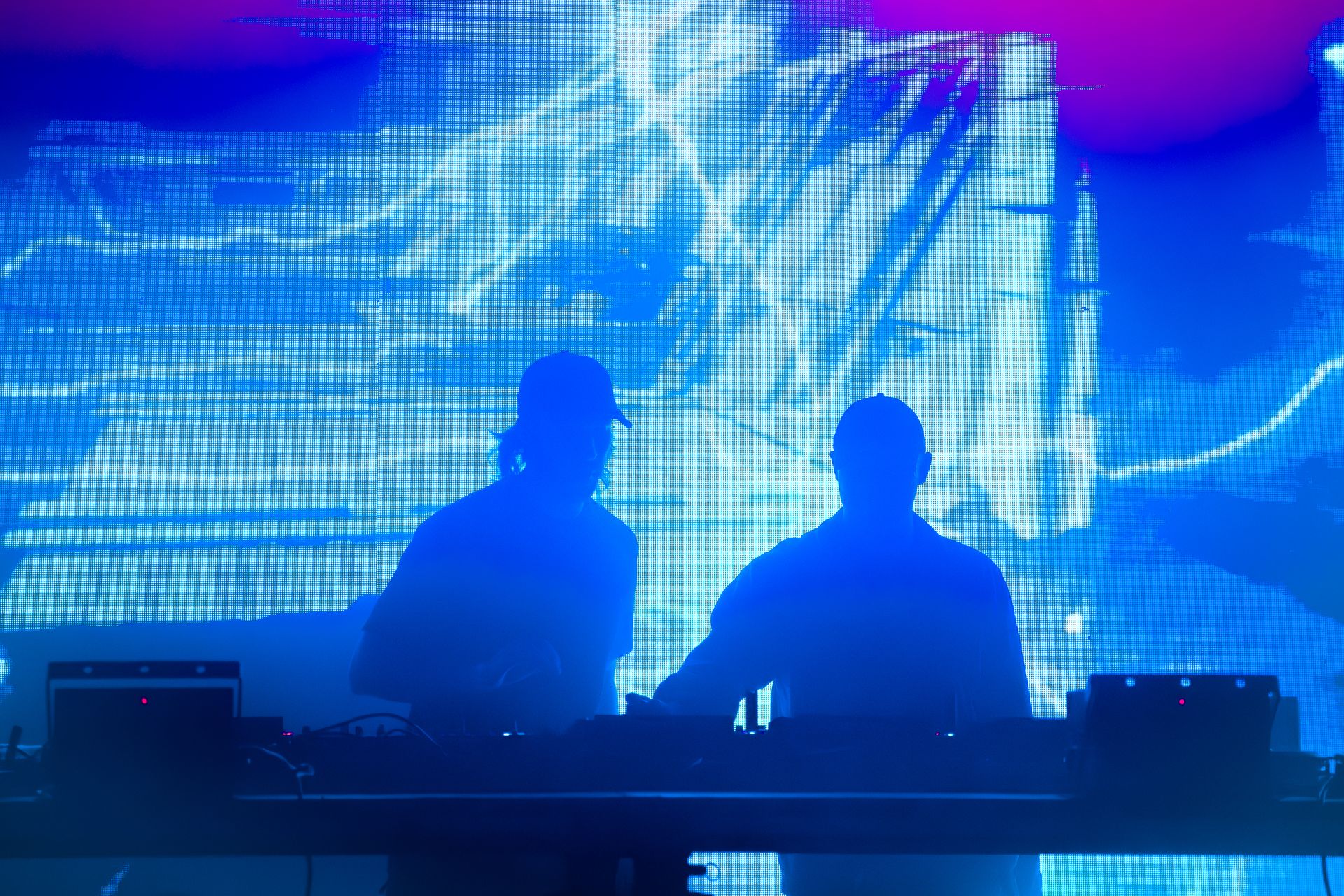 Two men are sitting at a table in front of a large screen.