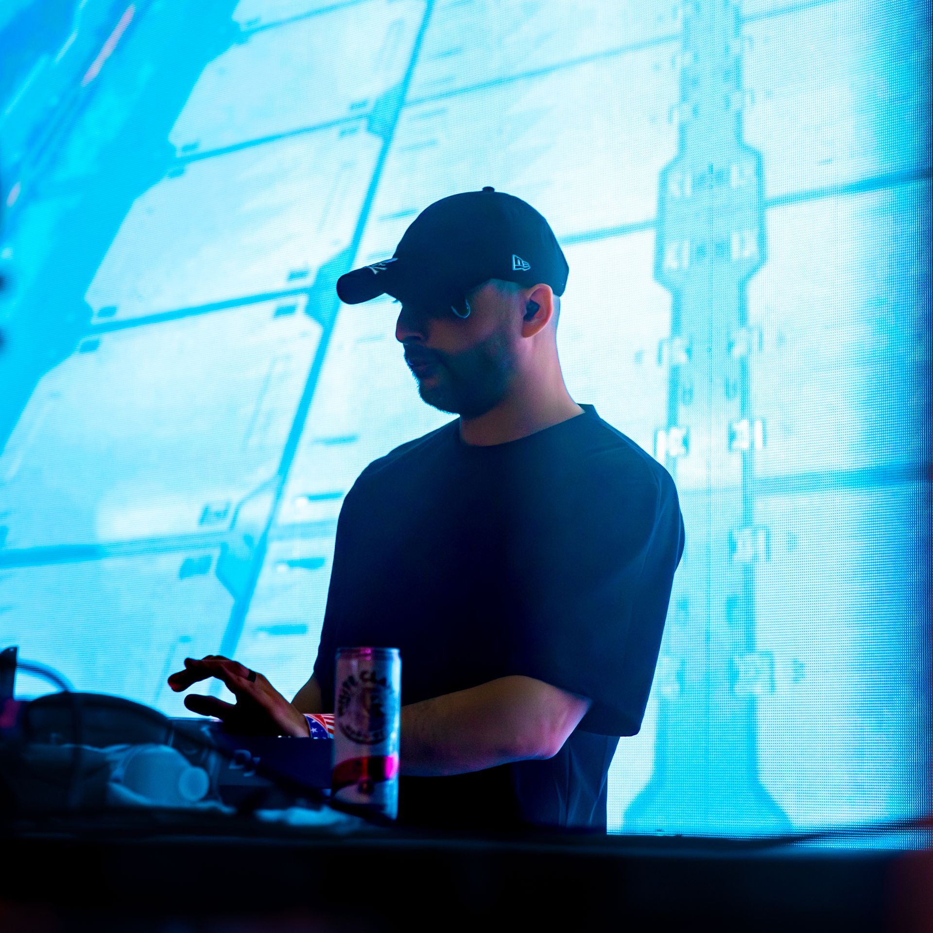 A man wearing a hat and sunglasses is standing in front of a large screen